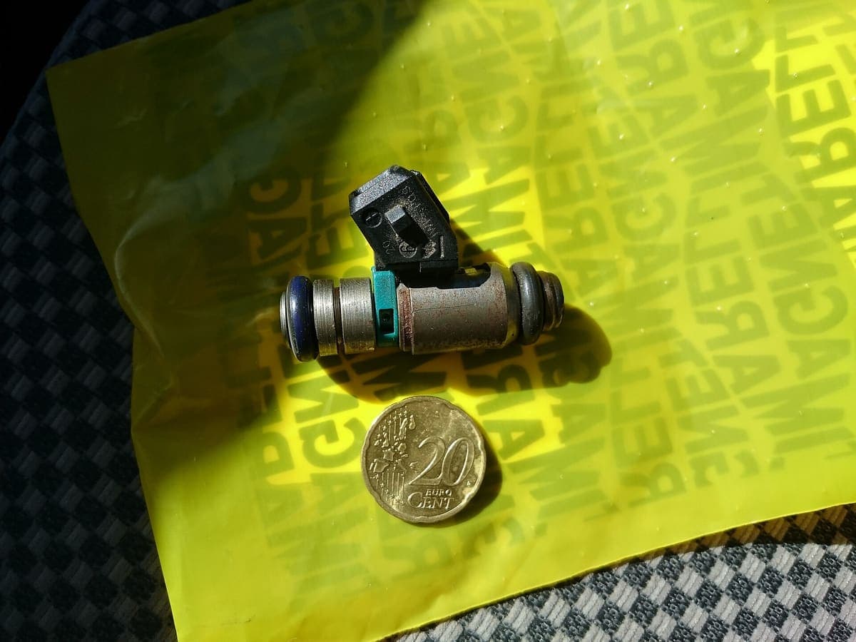 A car fuel injector removed from an engine, photographed against a size reference.