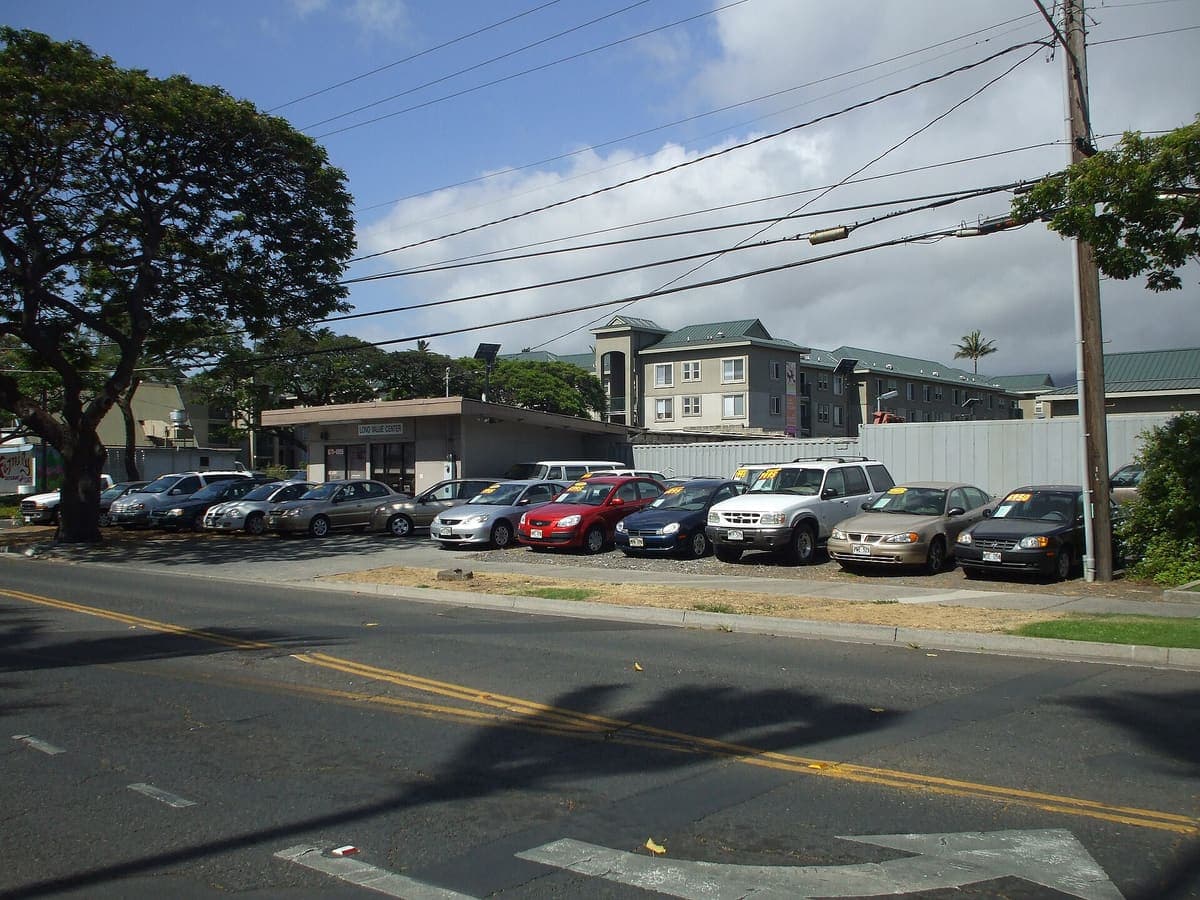 A used car lot with rows of second-hand vehicles parked side by side under signage