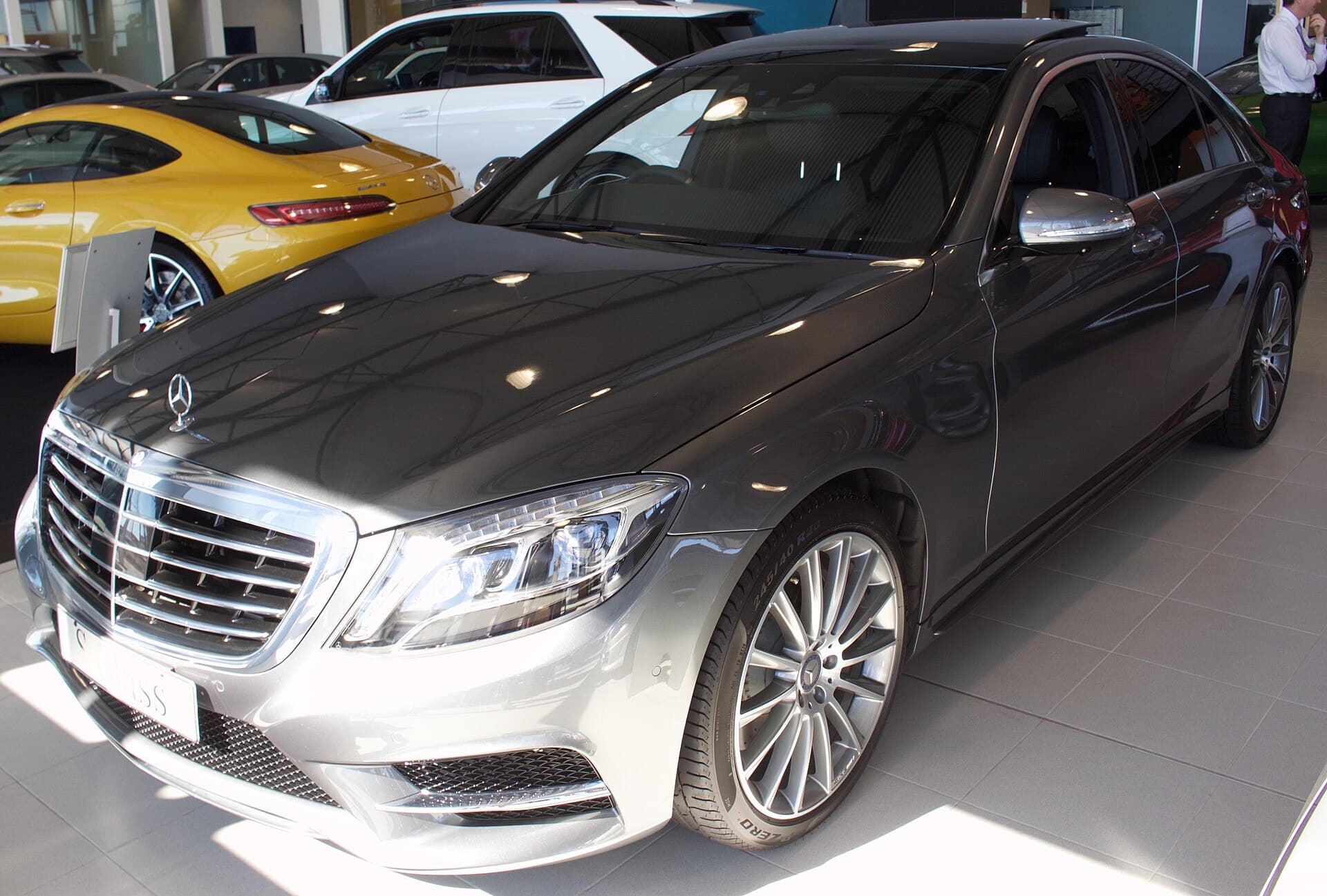 A grey Mercedes-Benz S-Class sedan with AMG Line styling inside a car showroom.