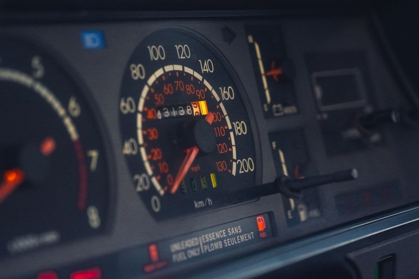 The analogue speedometer and mechanical odometer of an older car's instrument cluster, lit in orange.