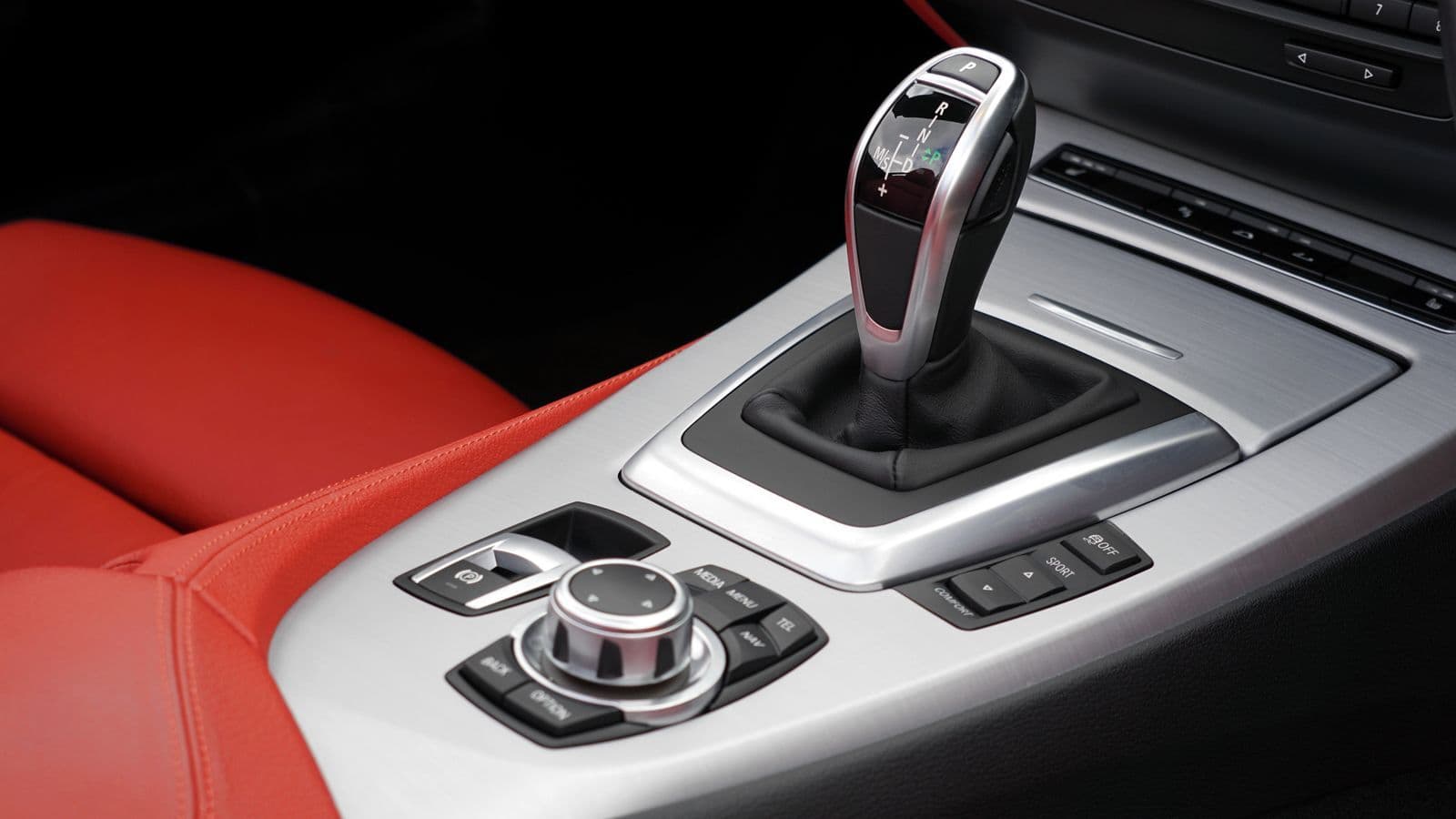 The chrome automatic gear selector and brushed-metal centre console of a car with red leather seats.