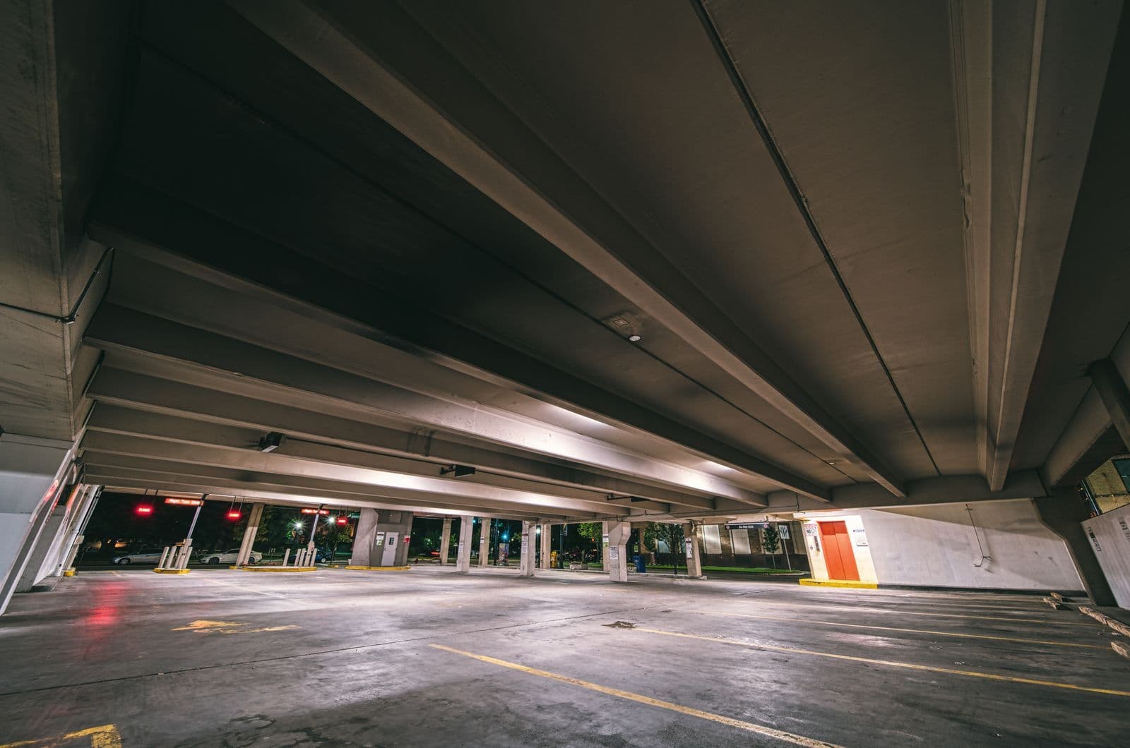 An empty, dimly lit multi-storey car park at night with bare marked bays and a low concrete ceiling.