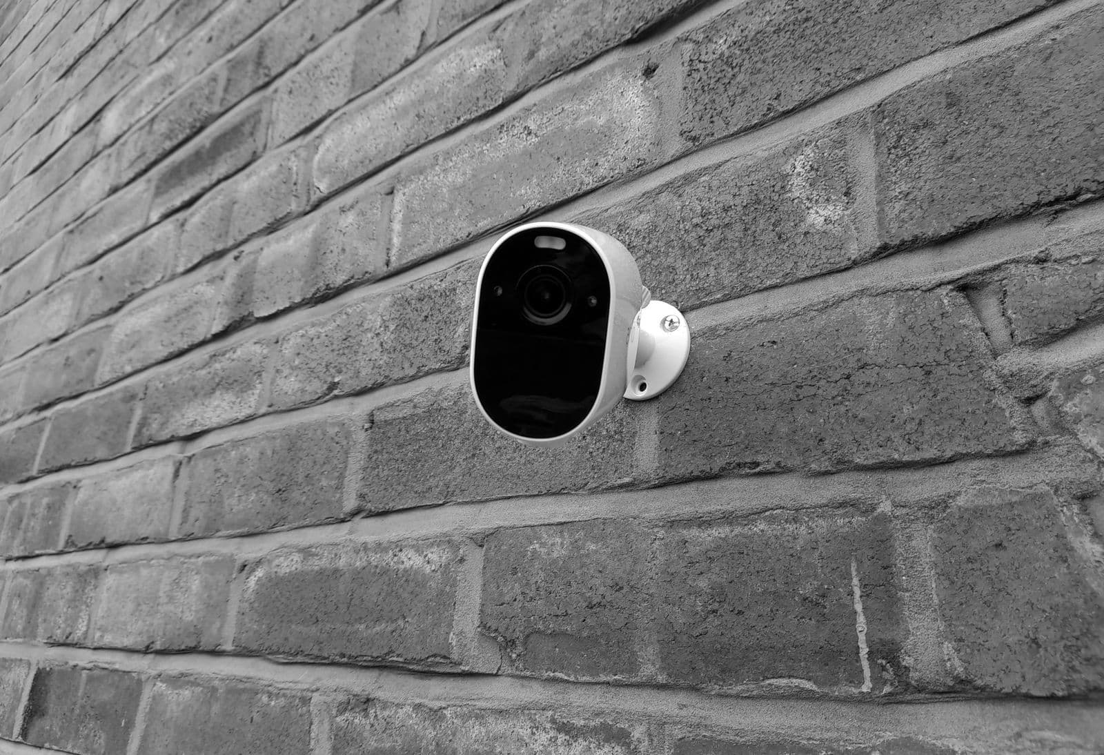 A black-and-white photo of a small wireless security camera mounted on a brick wall.