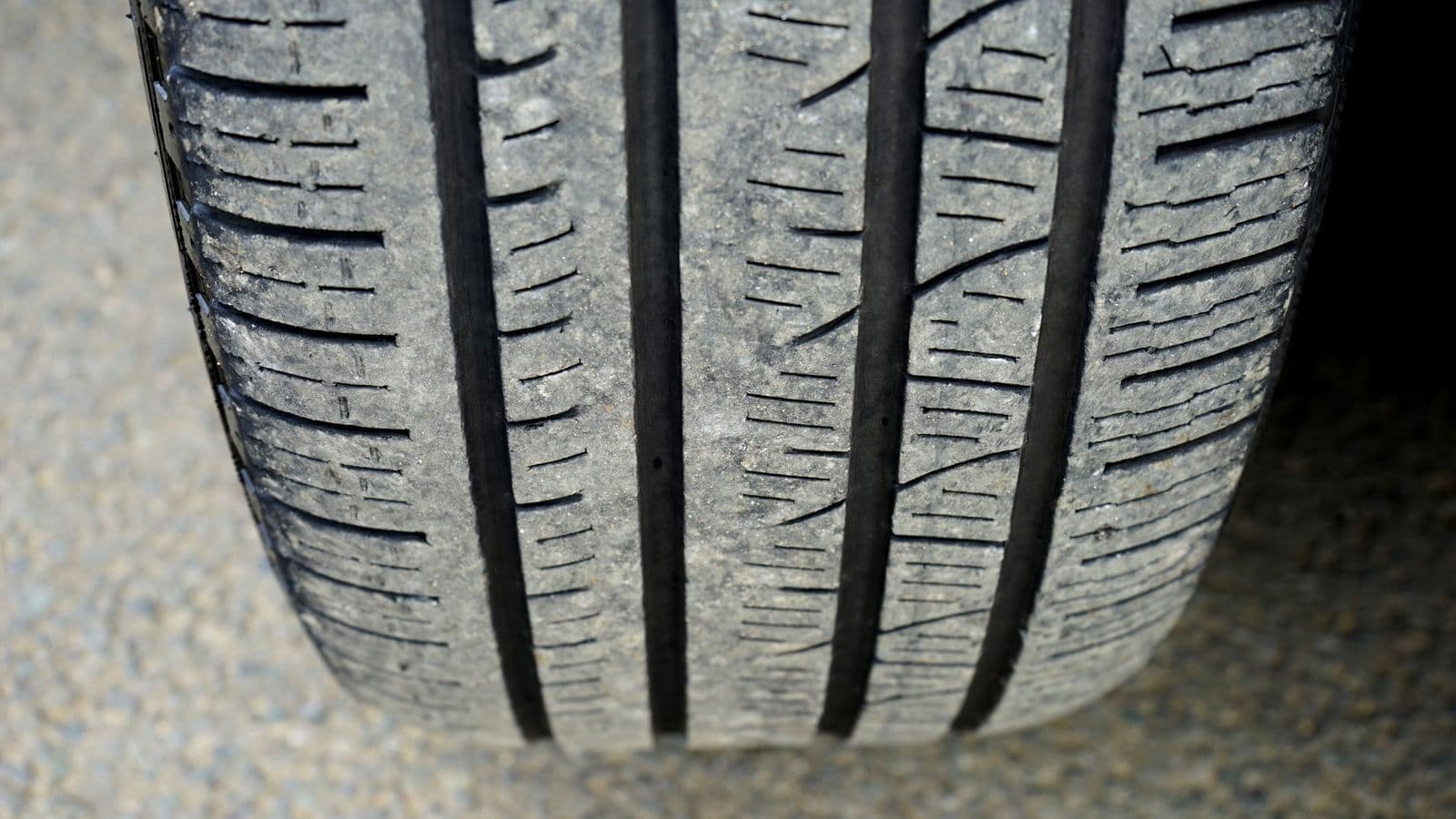 Extreme close-up of a car tyre's tread grooves and shoulder blocks where the rubber meets a concrete surface.