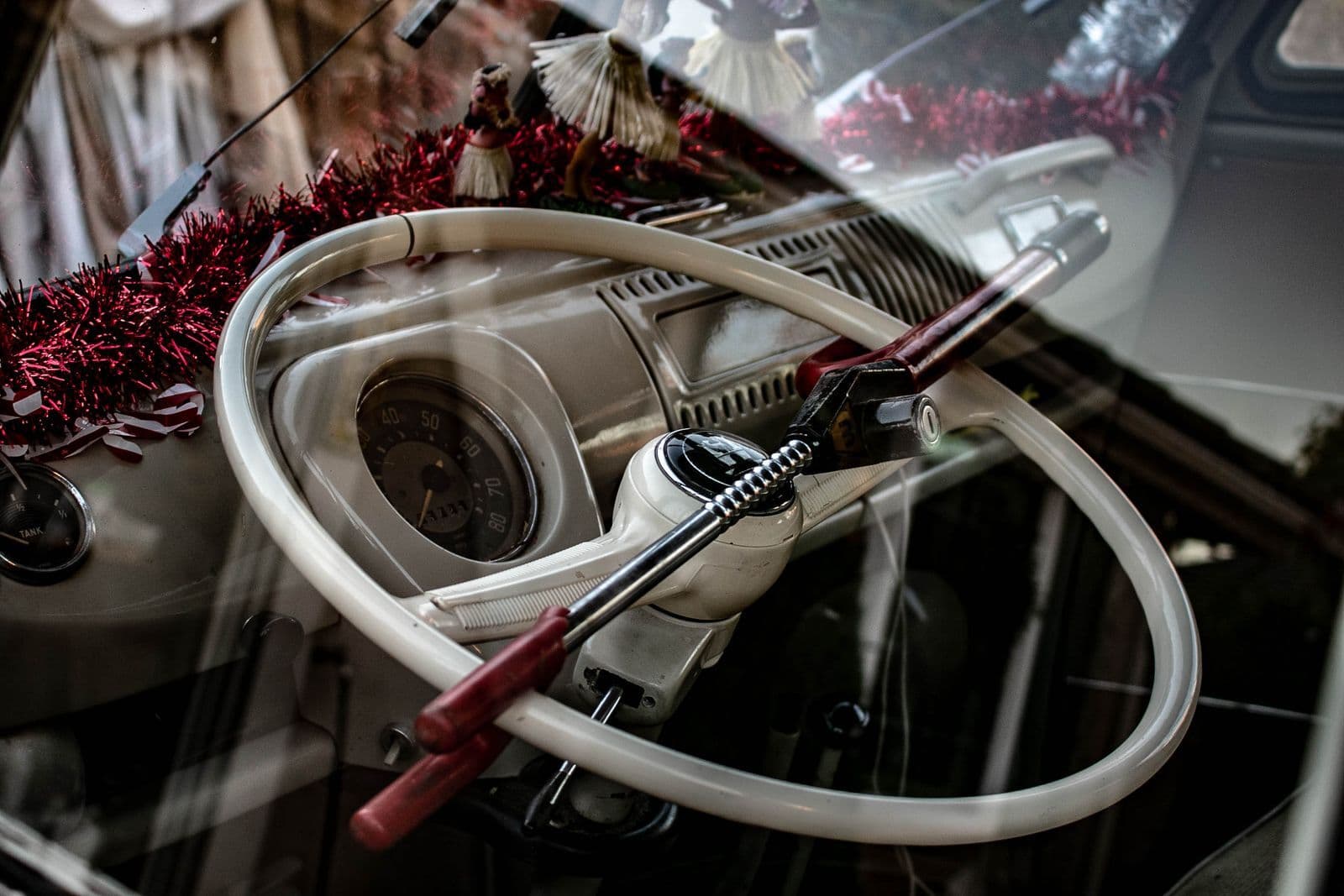 A red anti-theft lock clamped across the white steering wheel of a vintage van, seen through the window.