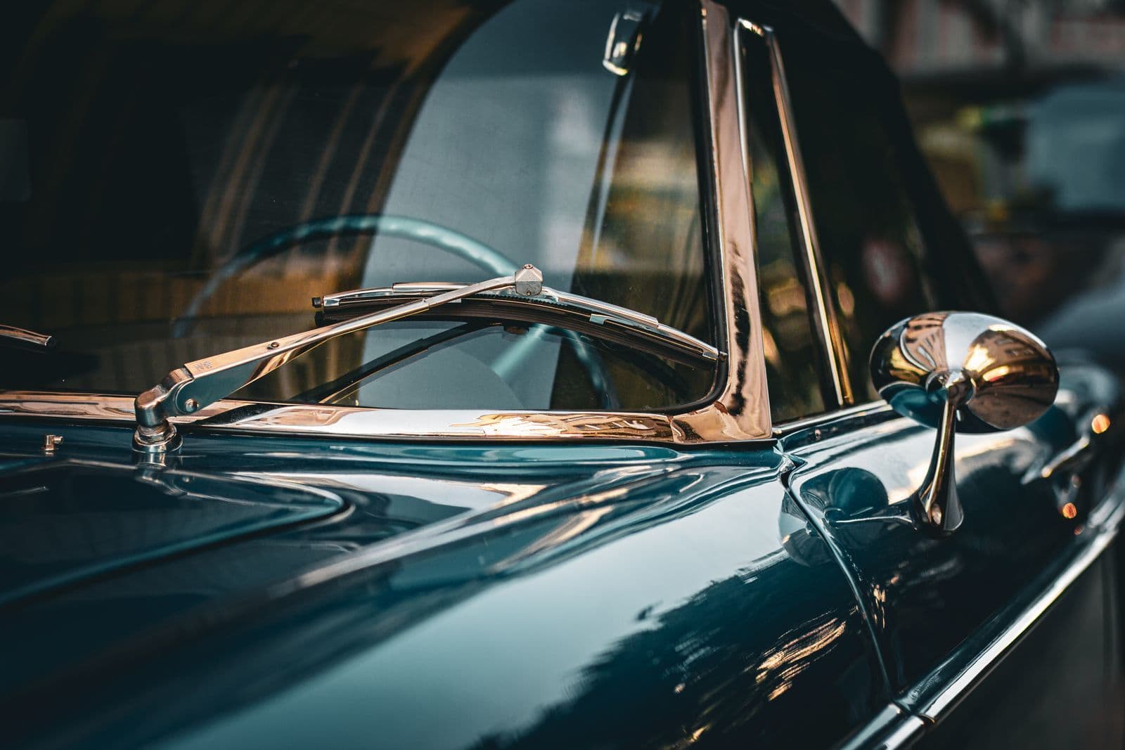 A close view of a dark green classic car's windscreen, chrome wiper arm and chrome wing mirror.
