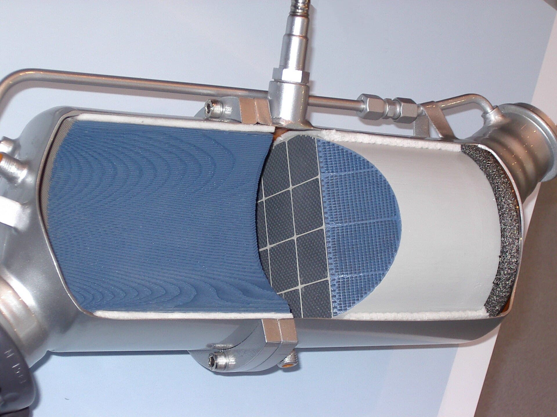 A cutaway display model of a diesel particulate filter, showing a blue ceramic catalyst section and a grey honeycomb filter inside a metal housing.