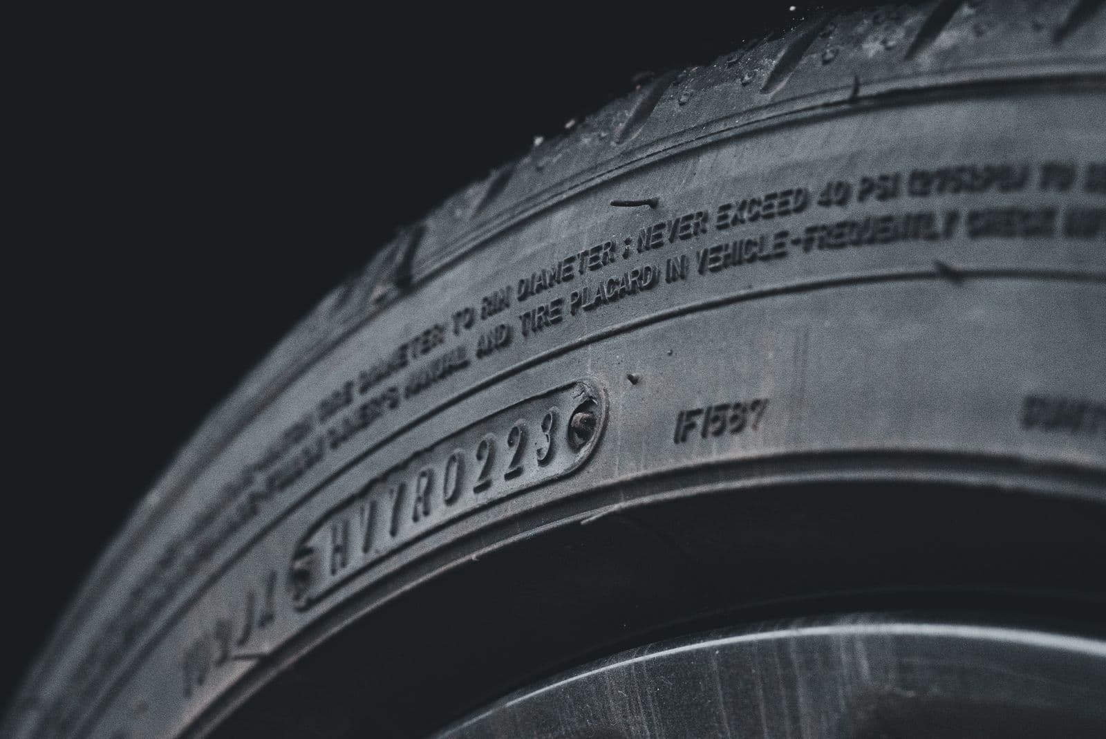 A close-up of a black tyre sidewall showing its moulded serial code and pressure warning text.