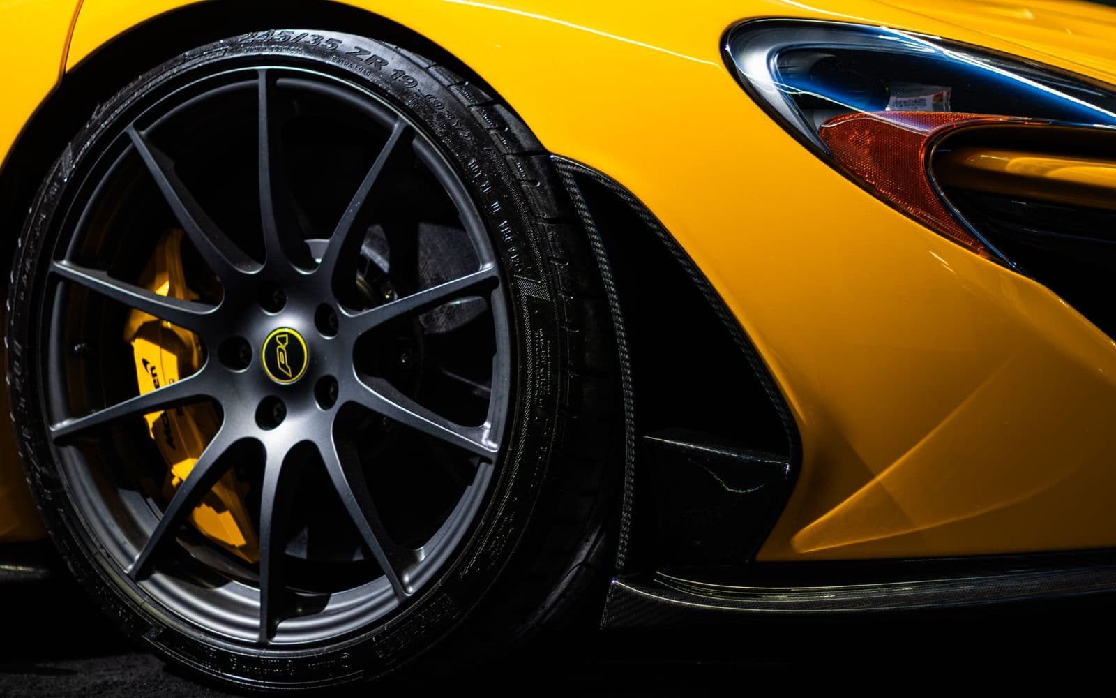 Close-up of the front wheel, yellow brake caliper and headlight of a yellow McLaren P1 against a dark background.