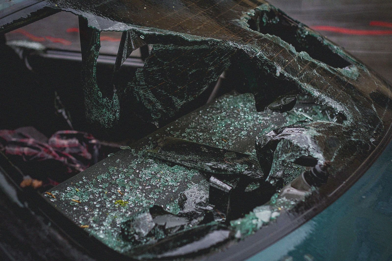 A car's shattered rear window, its safety glass broken into jagged sheets and fragments scattered across the parcel shelf.