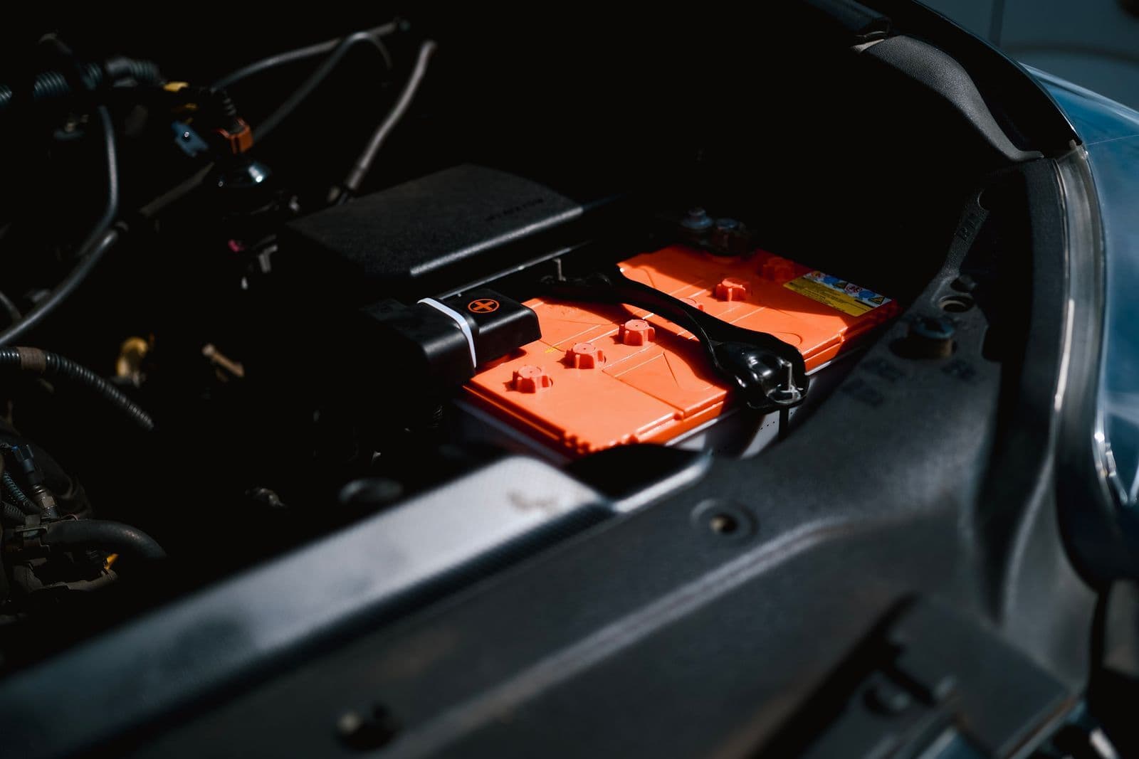 Orange high-voltage battery modules sitting in the engine compartment of an electric car under a raised bonnet.