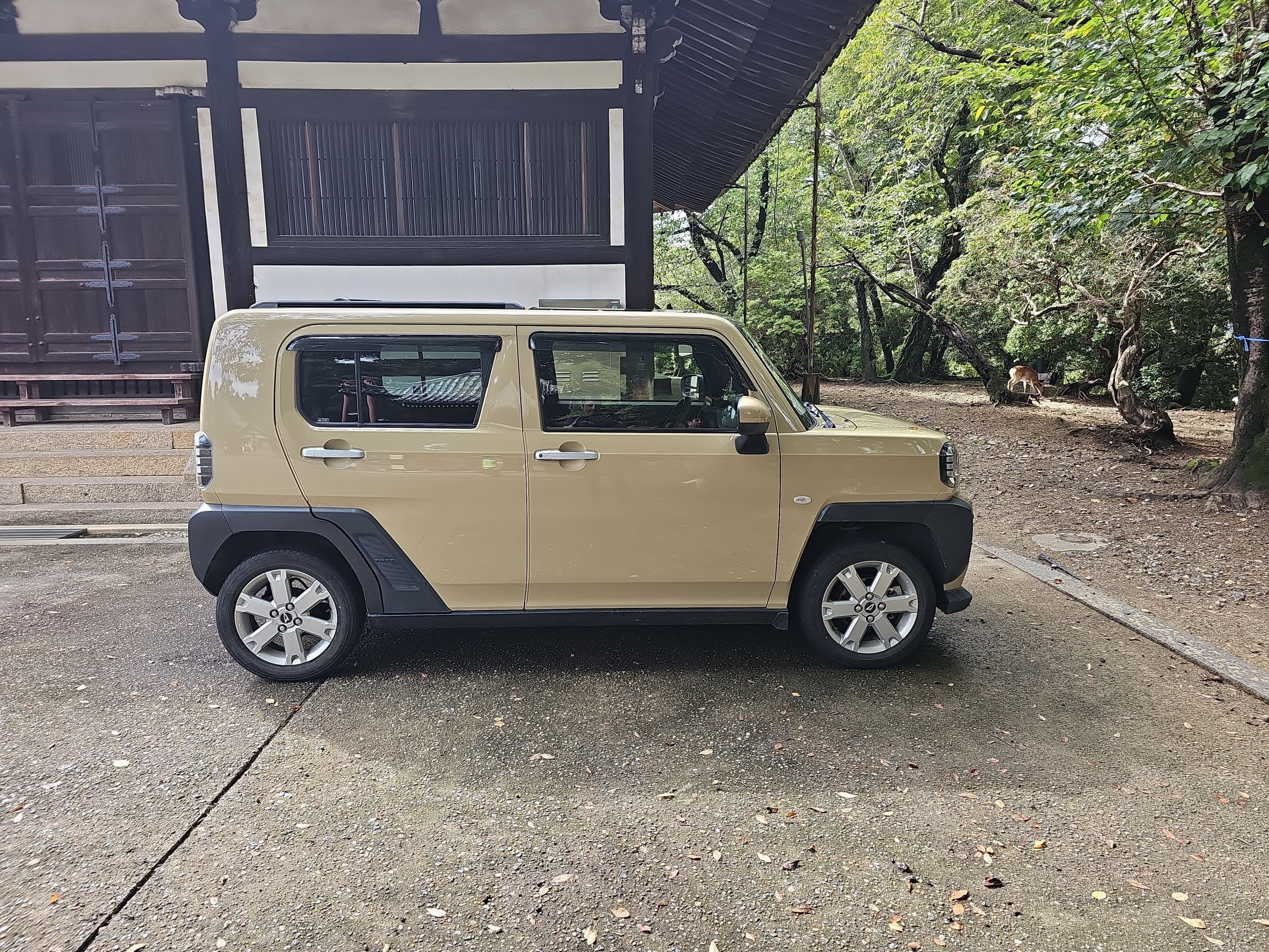 A beige compact kei car parked beside a traditional wooden building in Nara.