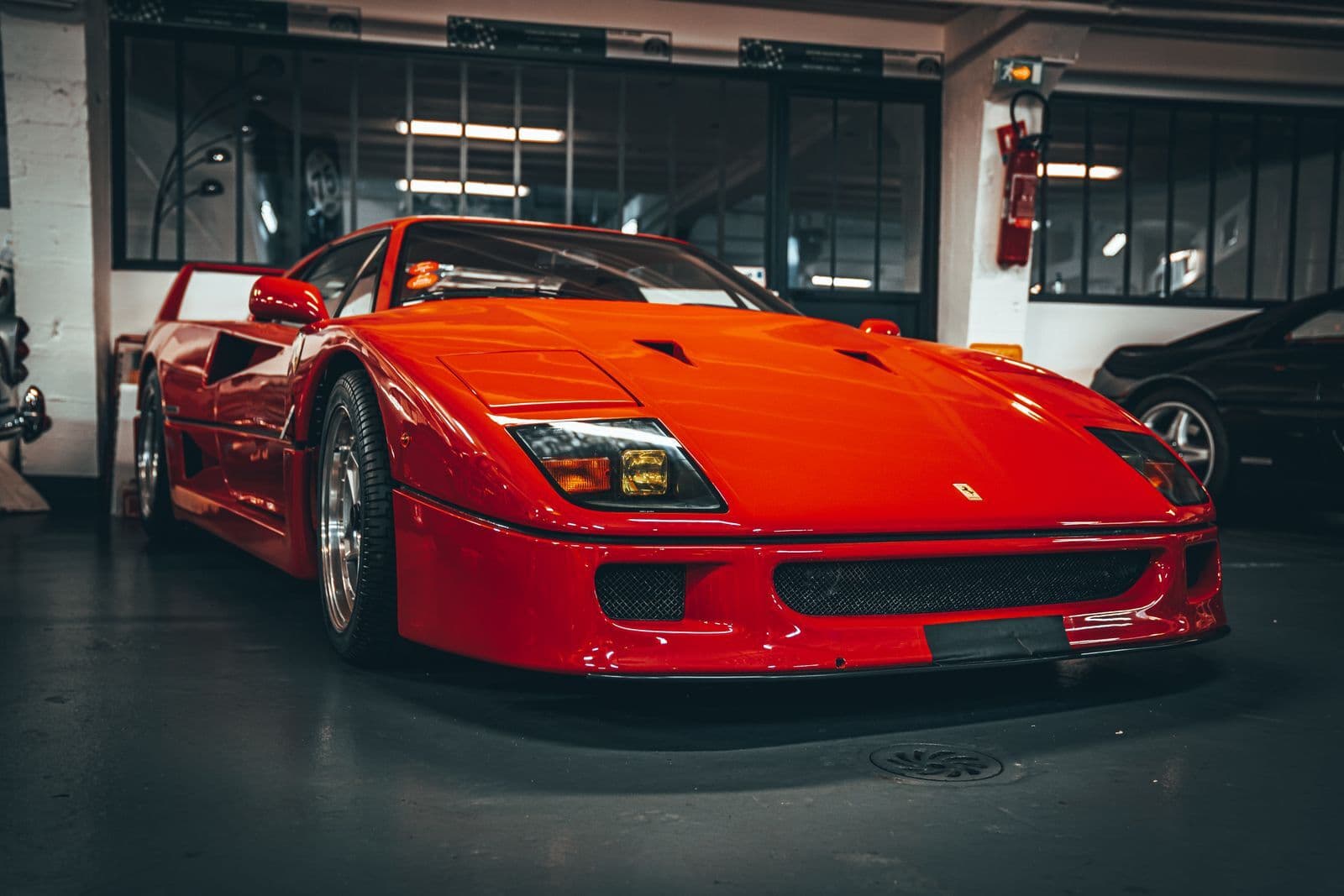 A red Ferrari F40 parked in a dim indoor storage garage beside other cars.