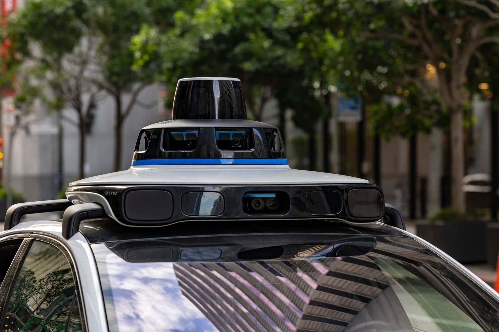 A close-up of the spinning sensor and camera pod mounted on the roof of a self-driving car on a tree-lined street.