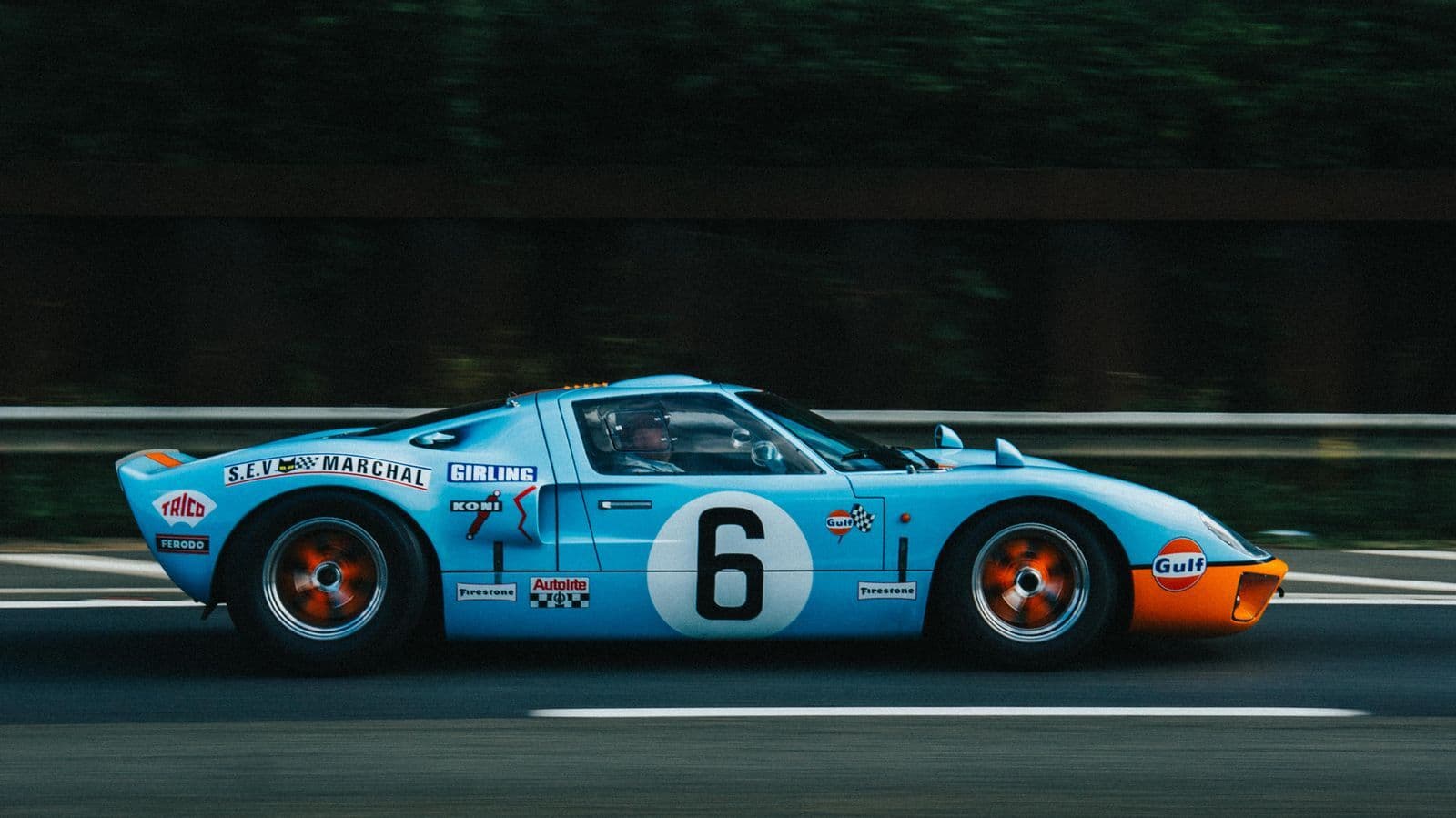 A light blue and orange GT40-style race car with the number 6 driving along a road.