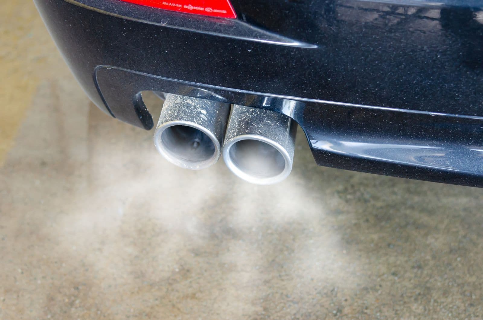 Pale exhaust smoke drifting from the twin chrome tailpipes of a dark car.