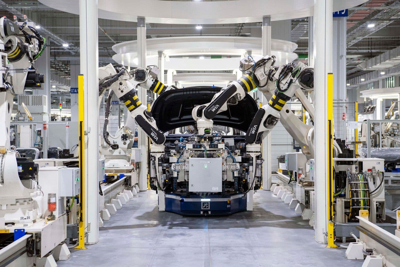 Large white robotic arms lower a car body onto a chassis on an automated assembly line inside a factory.