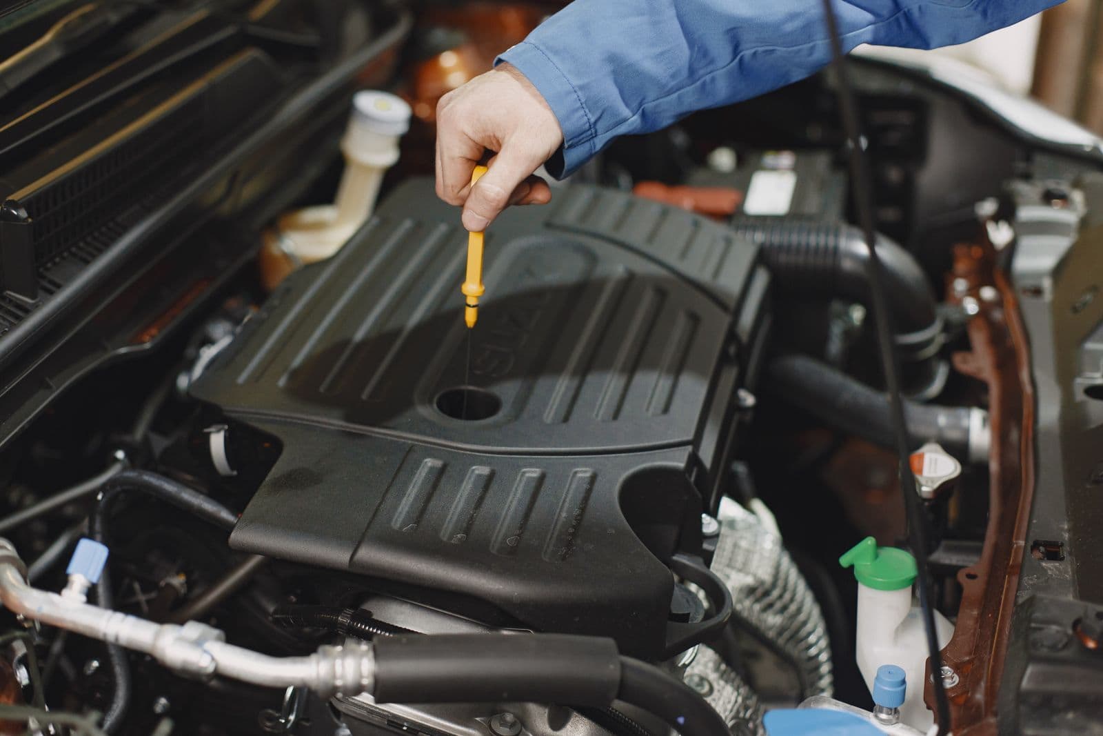 A hand withdrawing a yellow-handled dipstick from the top of a car engine under an open bonnet.
