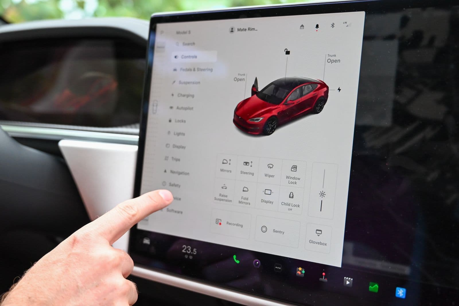 A finger reaching for a nested menu on a large touchscreen mounted in a car's dashboard.