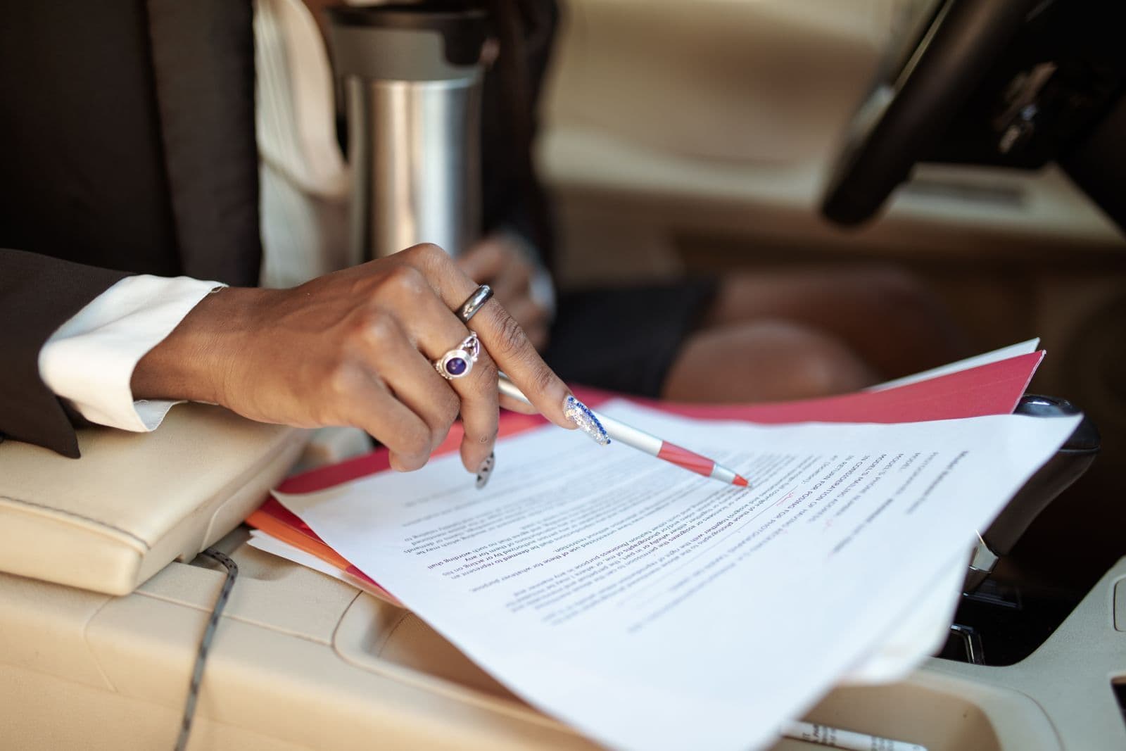 A person in a suit points a pen at a printed multi-page document resting on the centre console inside a car.