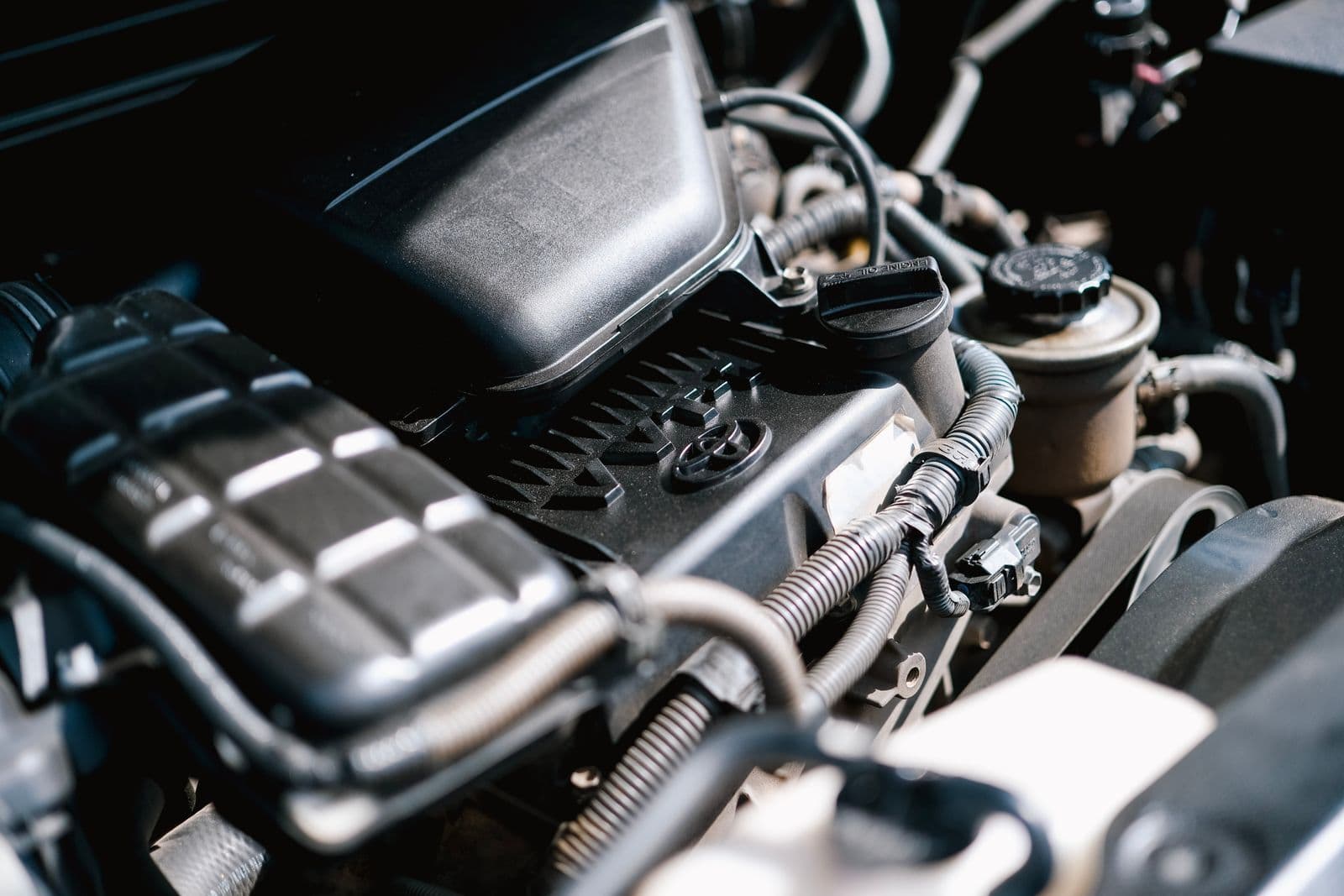 A close-up of a modern engine bay showing plastic covers, a coolant reservoir and bundled wiring looms in sunlight.