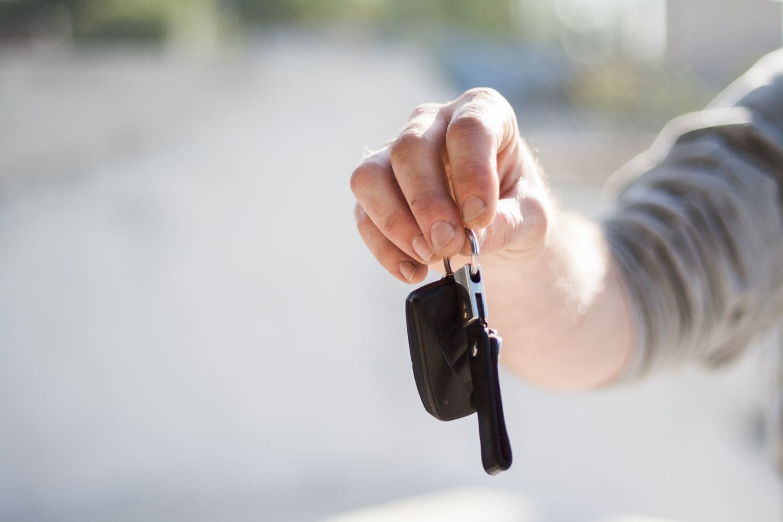 A hand holds out a car key on a key ring against a softly blurred background.
