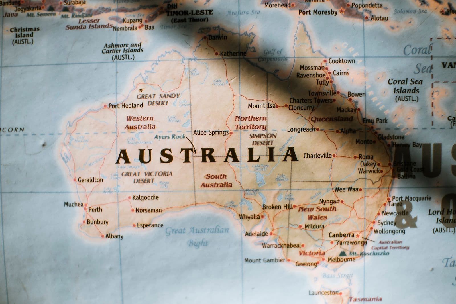A softly lit paper wall map of Australia showing the state names, major cities and surrounding seas.