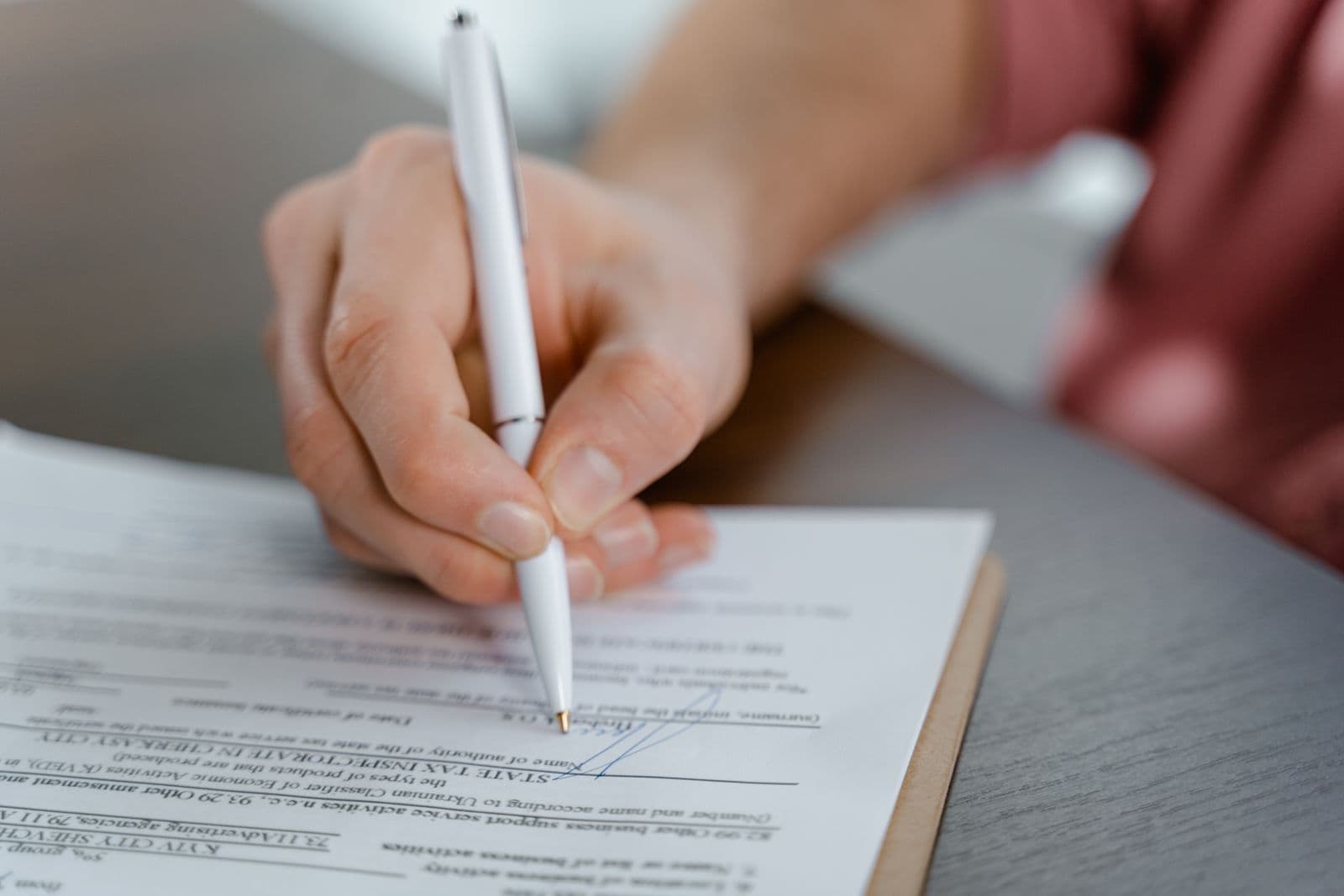 A hand holding a white pen, about to sign a printed form on a clipboard.