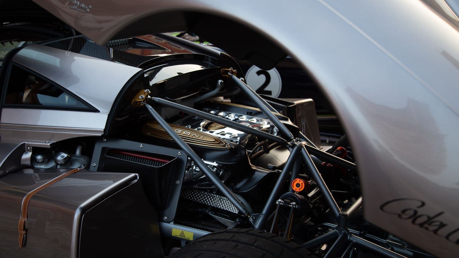 The exposed rear engine bay of a silver hypercar, its twelve-cylinder engine framed by a tubular subframe and carbon bodywork.