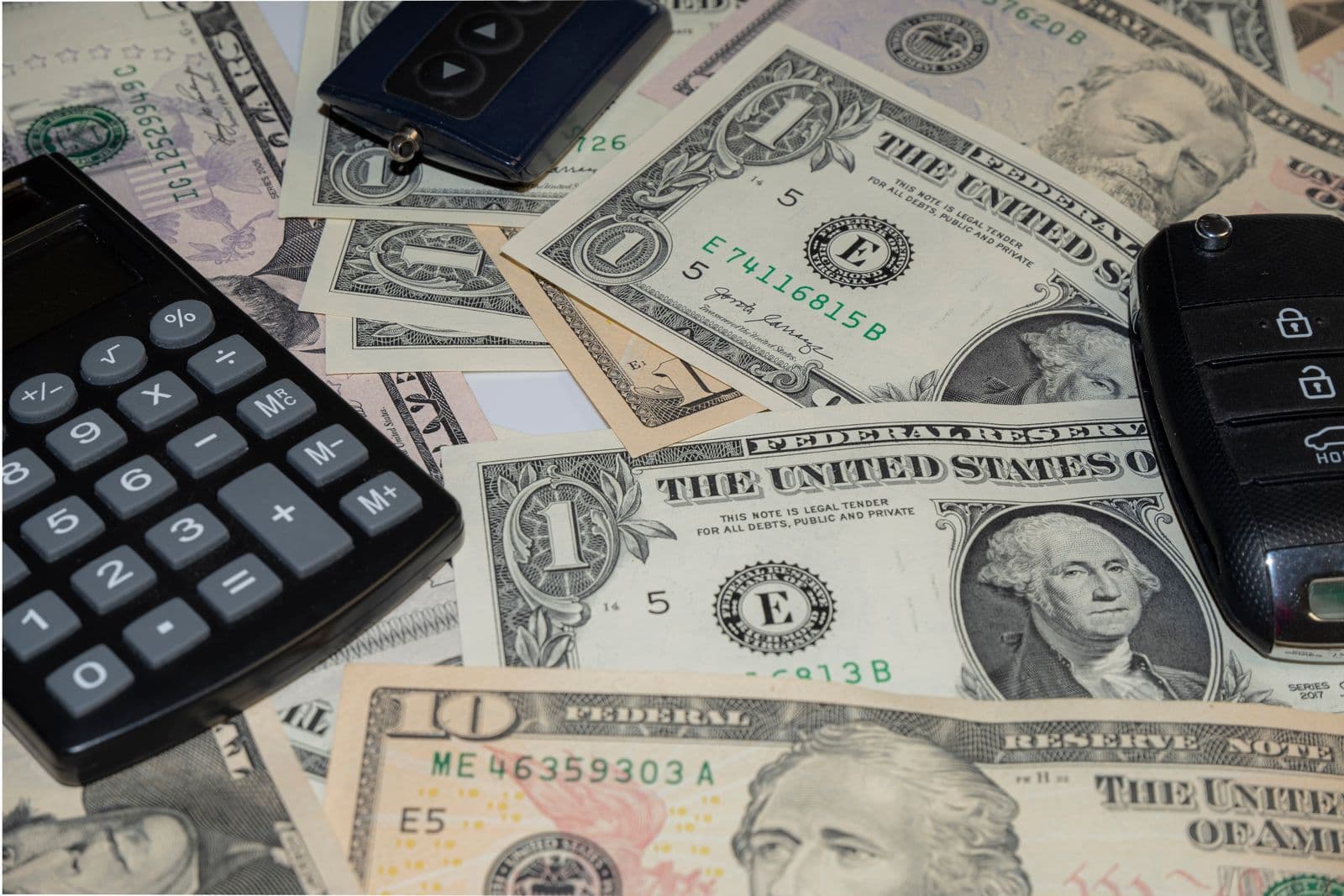 Two car key fobs and a black calculator lying on a spread of banknotes.