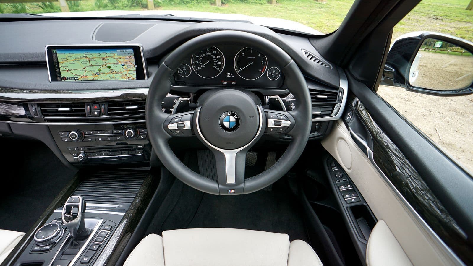 The cabin of a right-hand-drive car, with the steering wheel and instrument cluster on the right and the centre console and screen to the left.