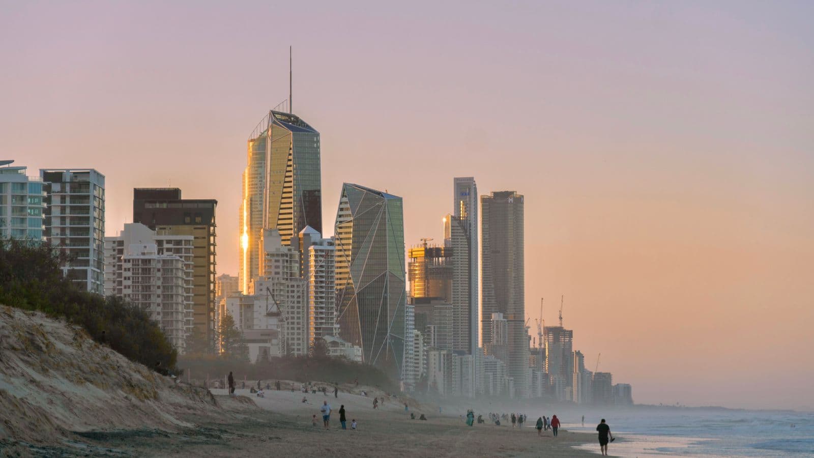 High-rise towers lining a beach at sunset, with people walking along the sand and surf.