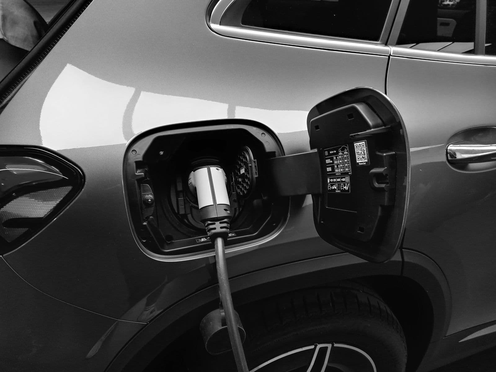 A black-and-white close-up of a charging plug inserted into the open charge port on the rear flank of an SUV.