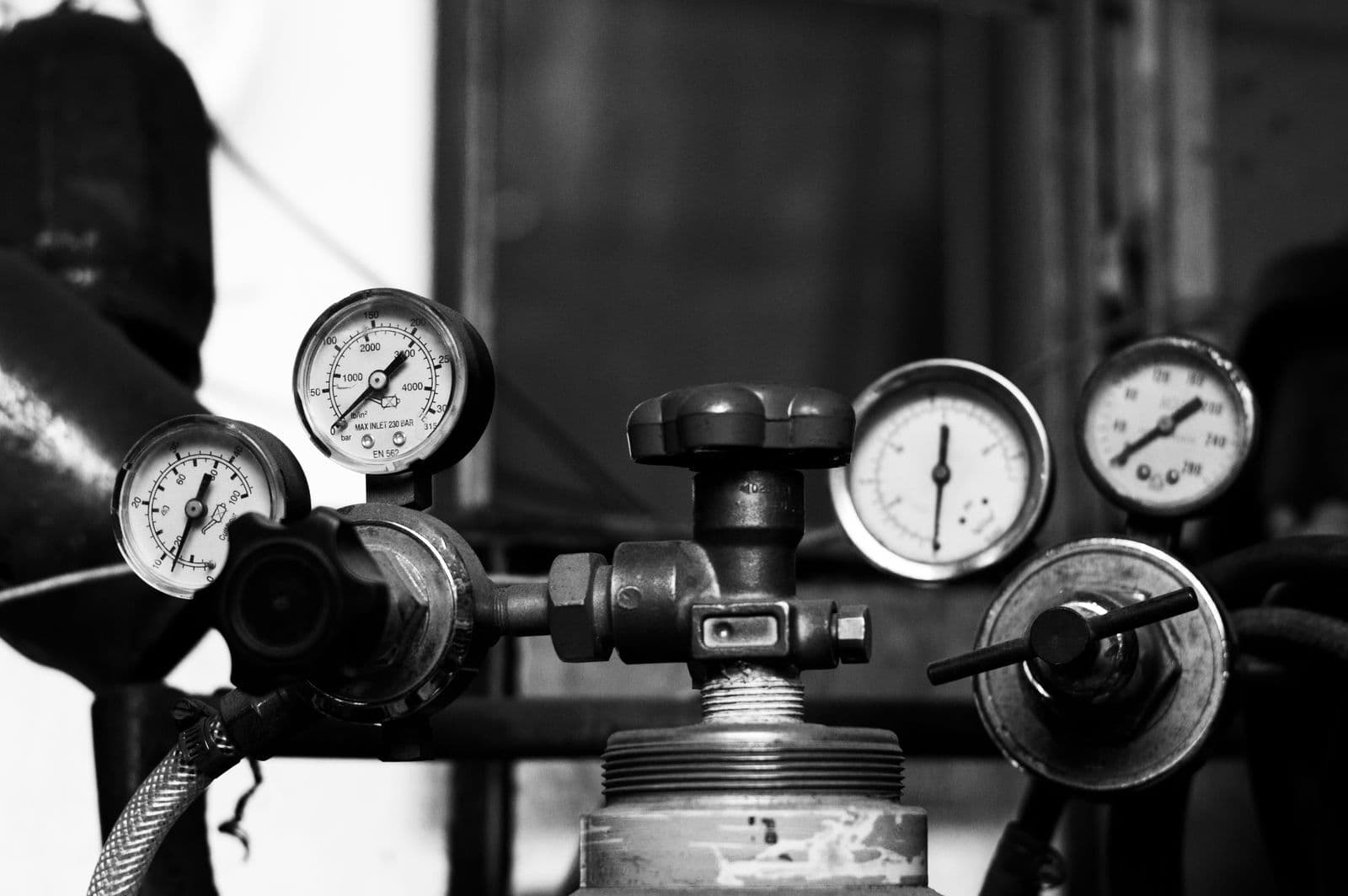 A black-and-white close-up of pressure gauges and a regulator valve on top of a gas cylinder.