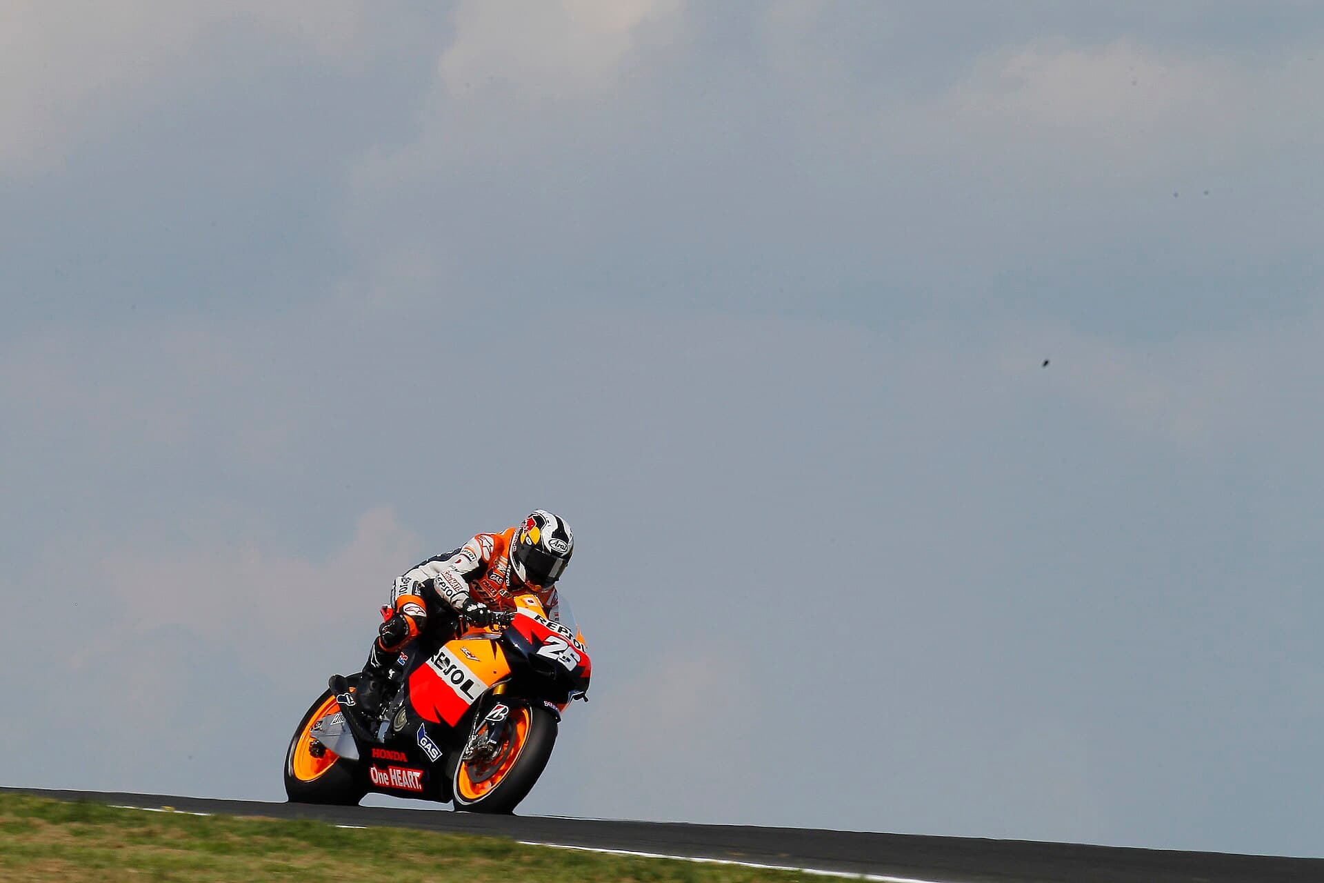 A Repsol Honda MotoGP bike crests a rise at Phillip Island with the rider tucked in against a grey sky.