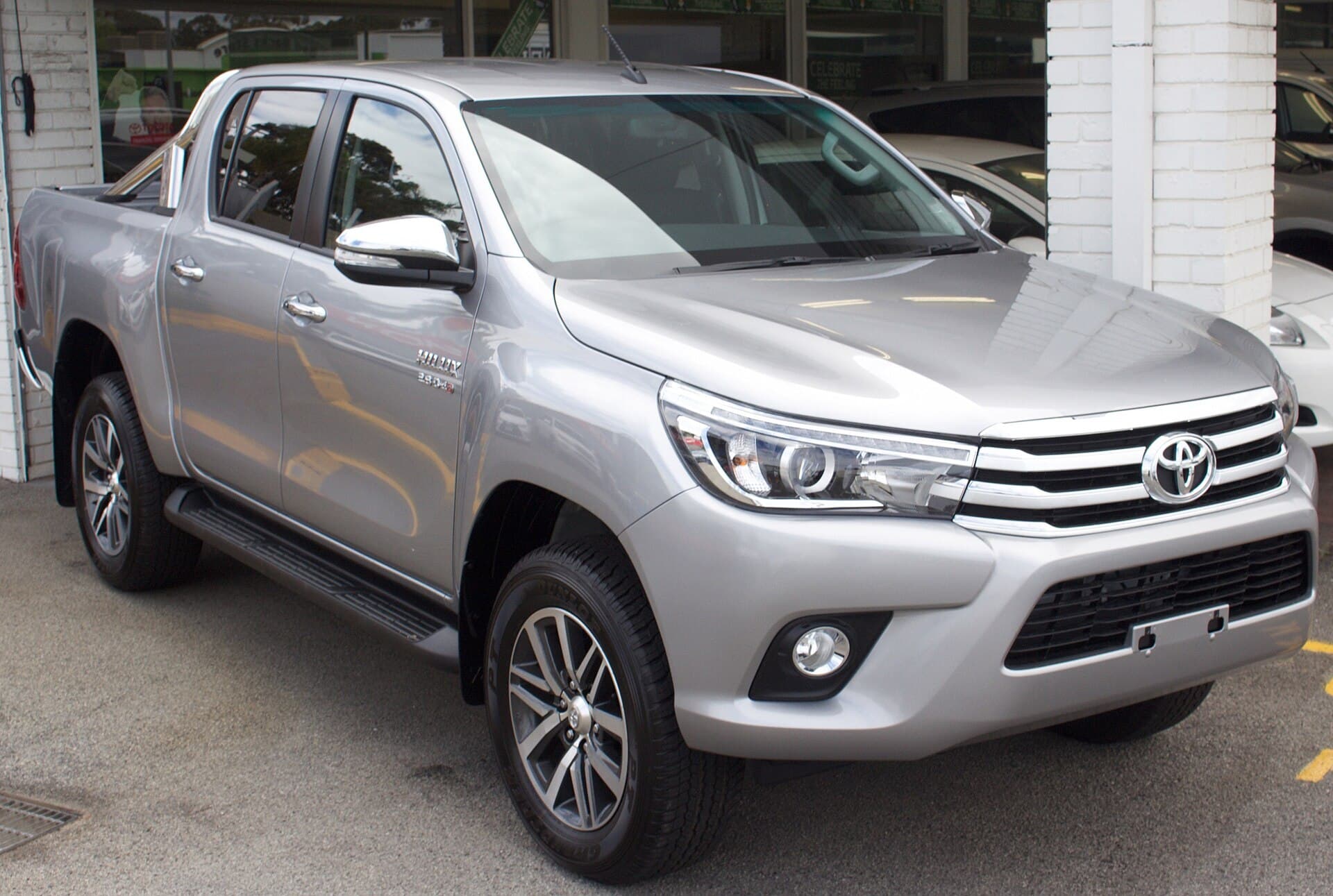 A silver Toyota HiLux SR5 dual-cab ute with no number plate, parked outside a dealership showroom.
