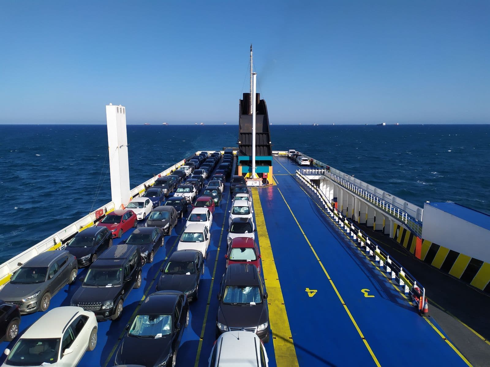 Rows of cars parked bumper to bumper on the open upper deck of a roll-on roll-off vehicle carrier at sea.