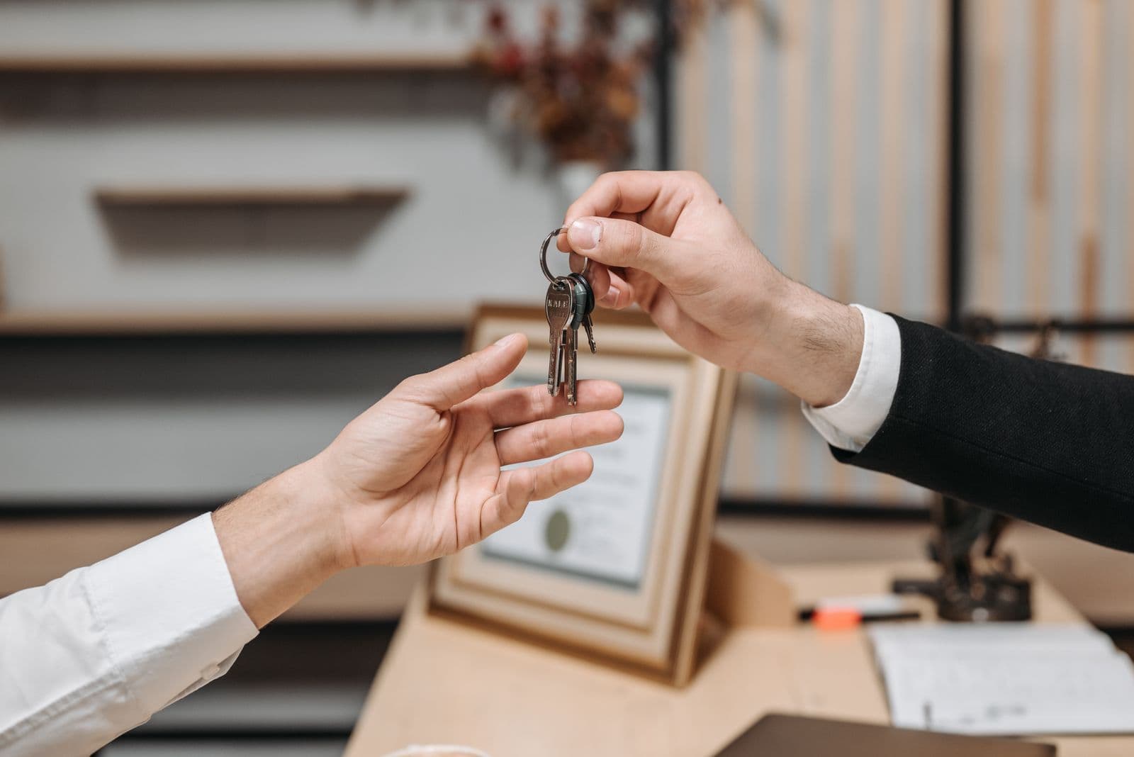 One person passing a bunch of keys into another person's open hand across a desk, with paperwork behind them.