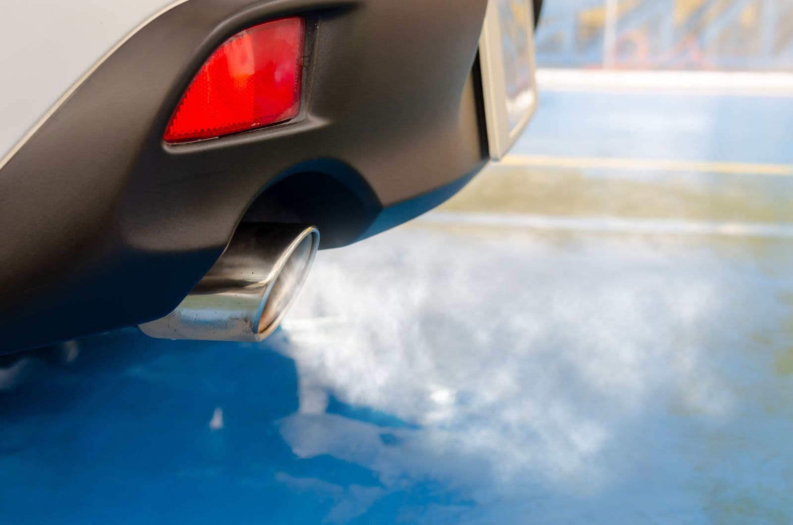 A close-up of a chrome exhaust tip under a car's rear bumper, with pale smoke drifting from it.