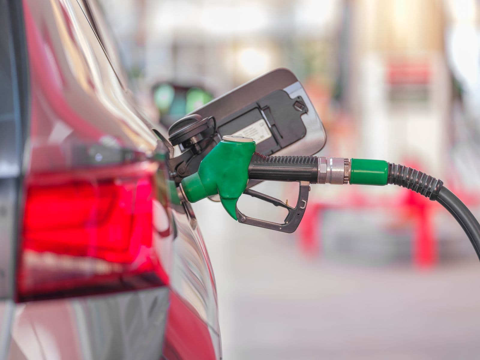 A green fuel nozzle sits in the open filler flap of a car at a service station.