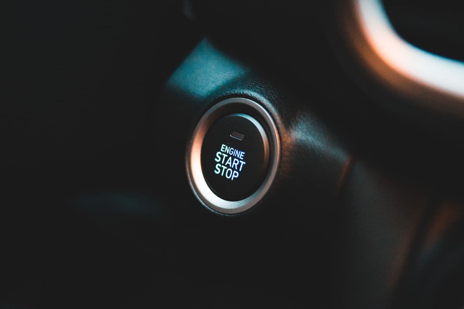 A glowing Engine Start Stop push button on a car's dark dashboard, beside the steering column.