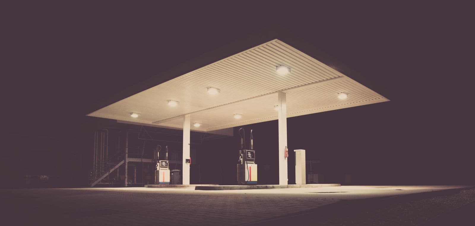 An empty, unbranded service station forecourt lit under its canopy at night, with two fuel pumps on the island.