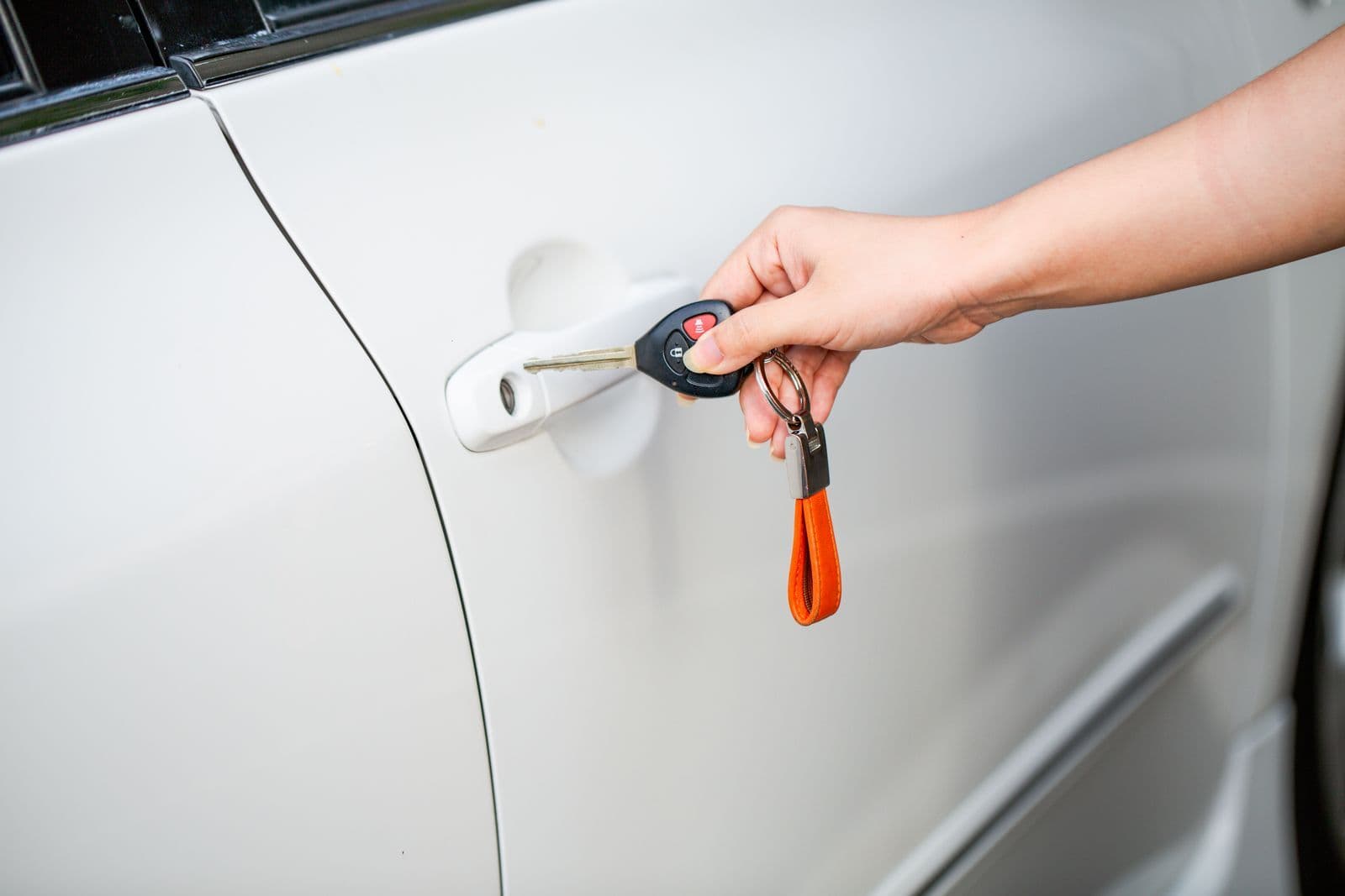 A hand turning a key with an orange keyring in the door lock of a white car.