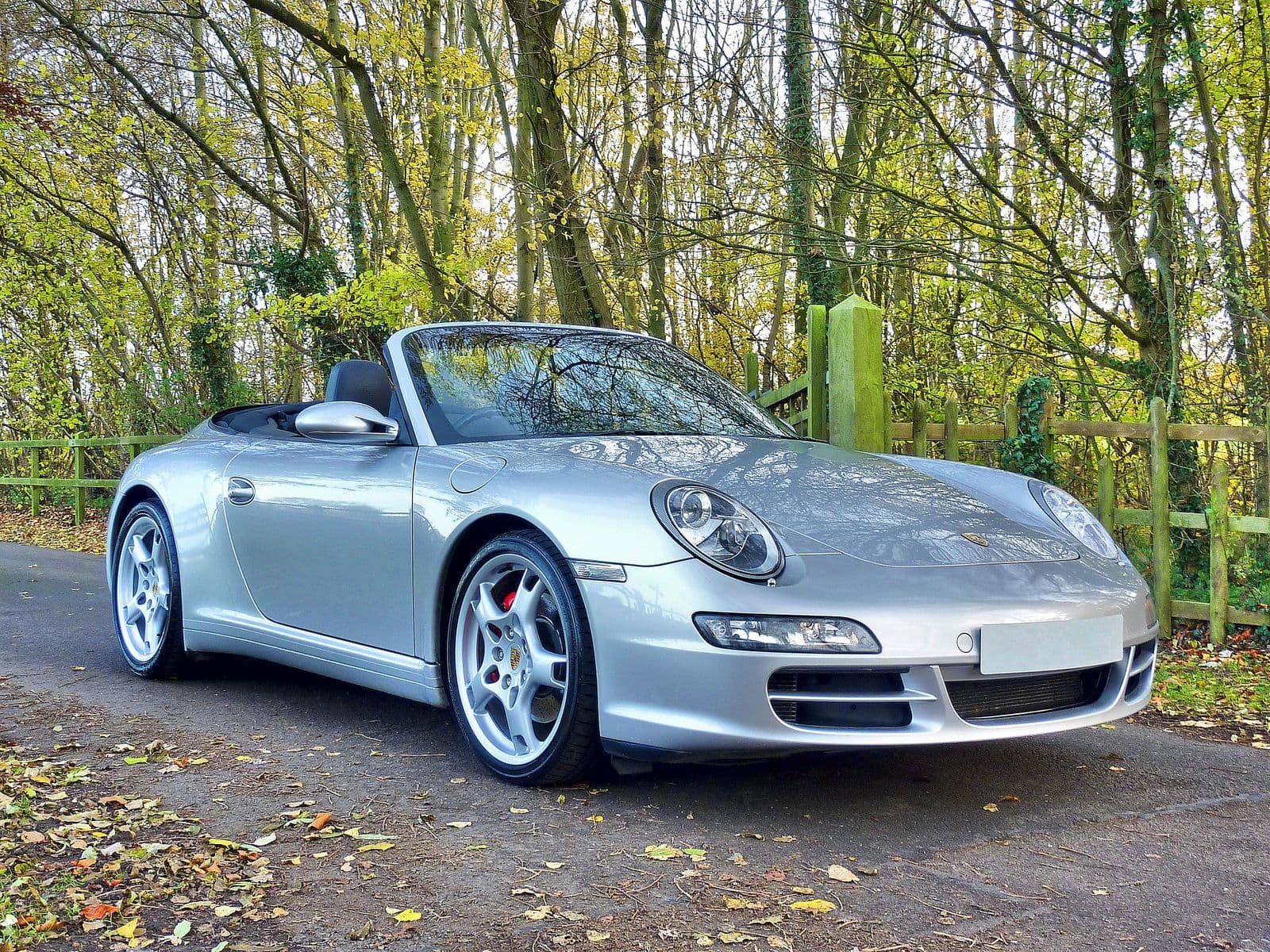 A silver Porsche 911 convertible parked on a leafy country lane in autumn.