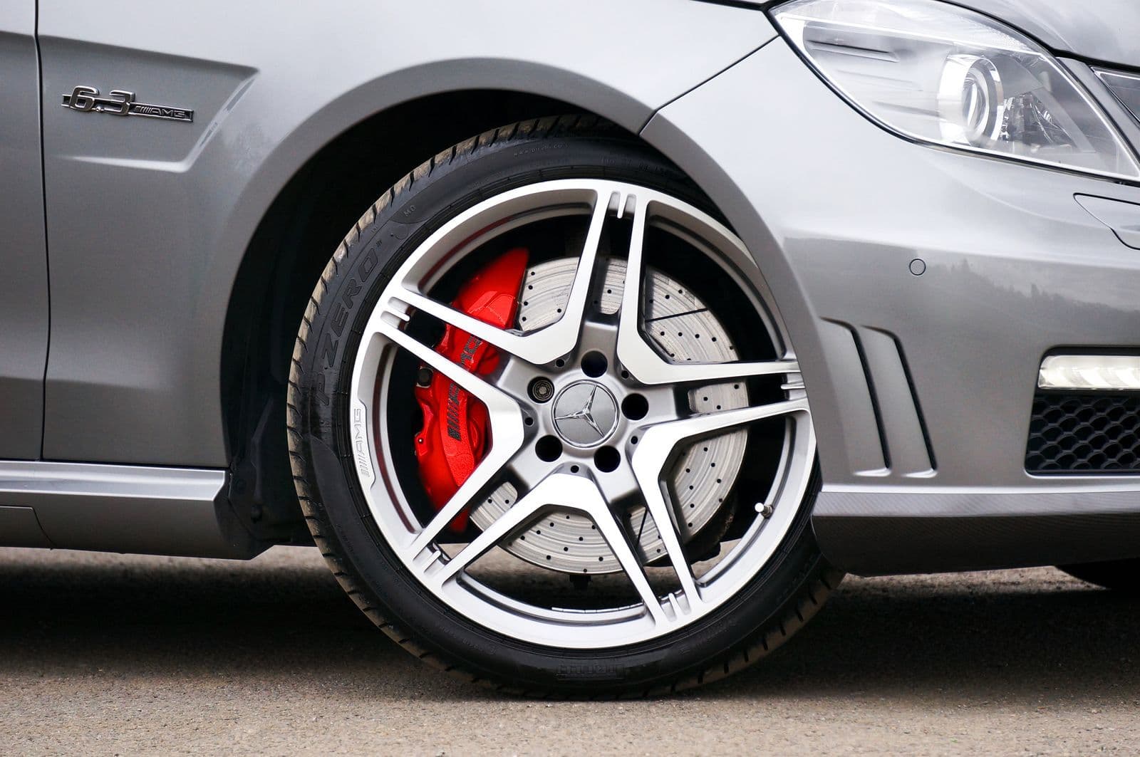 Close-up of a five-spoke polished alloy wheel on a silver car, with a red brake caliper and drilled disc visible behind the spokes.