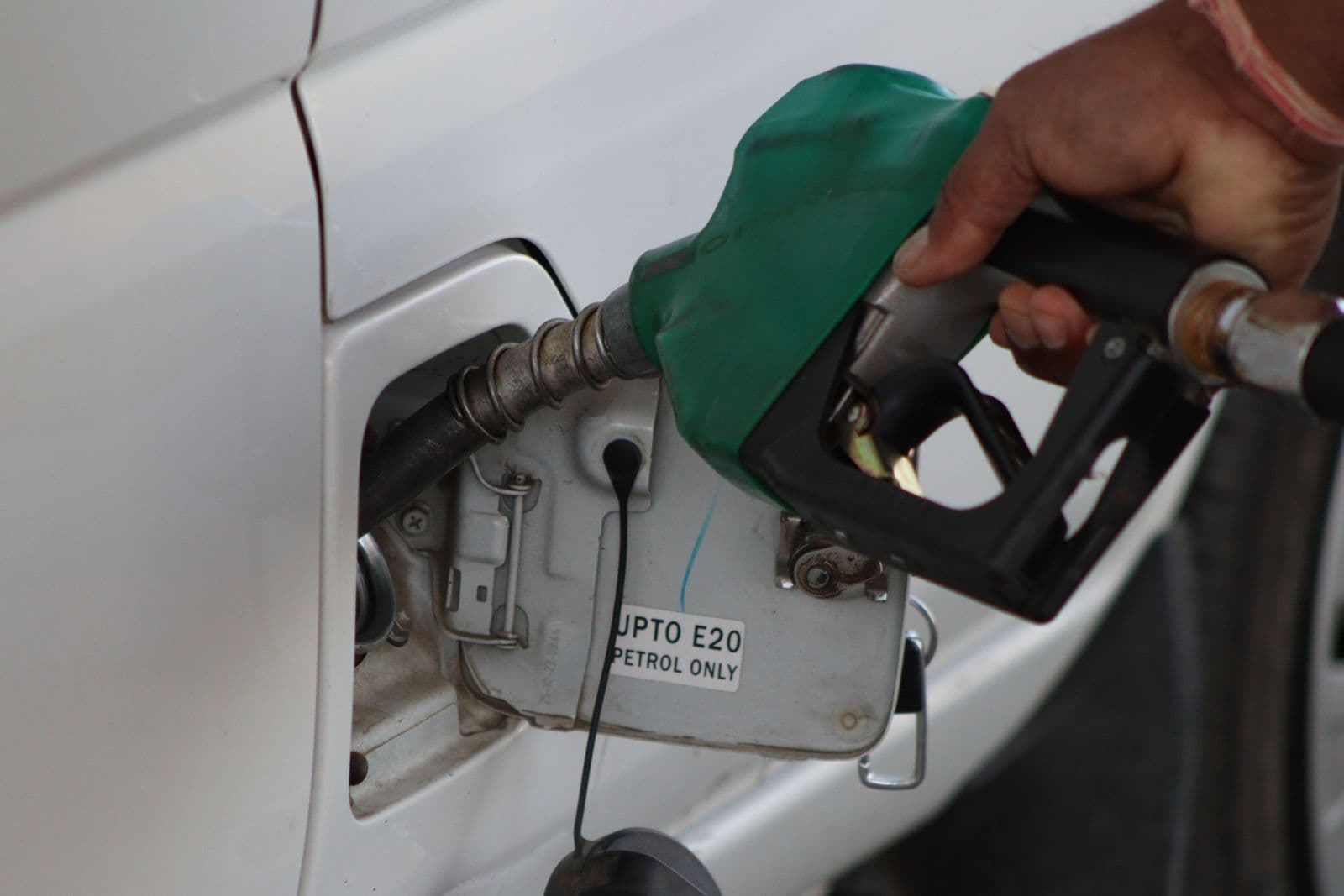 A hand holding a green fuel nozzle in a white car's filler, beside a label reading "Up to E20 petrol only".