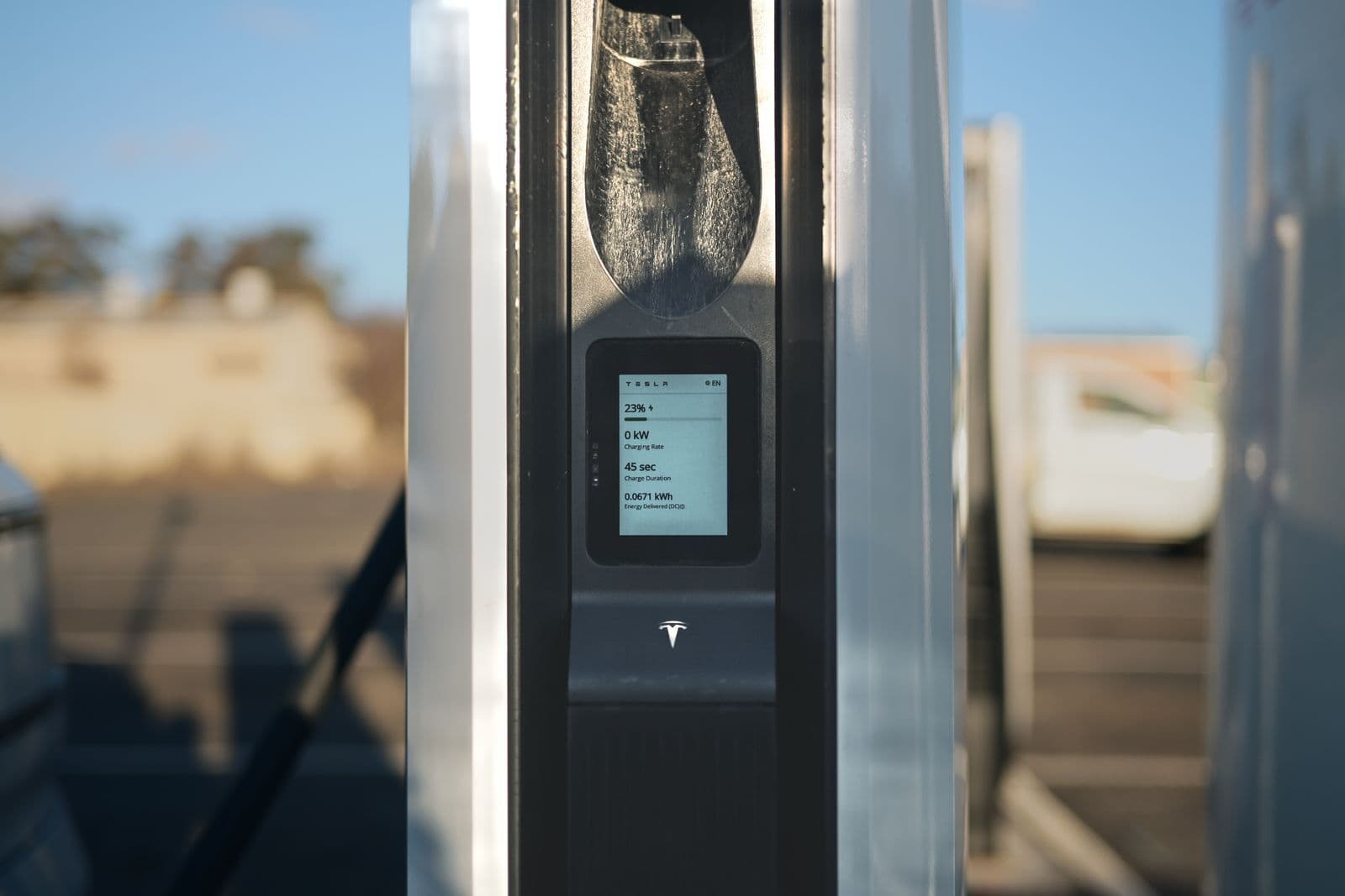 A public fast charger at an outdoor charging bay, its screen showing the charge level and power delivered mid-session.