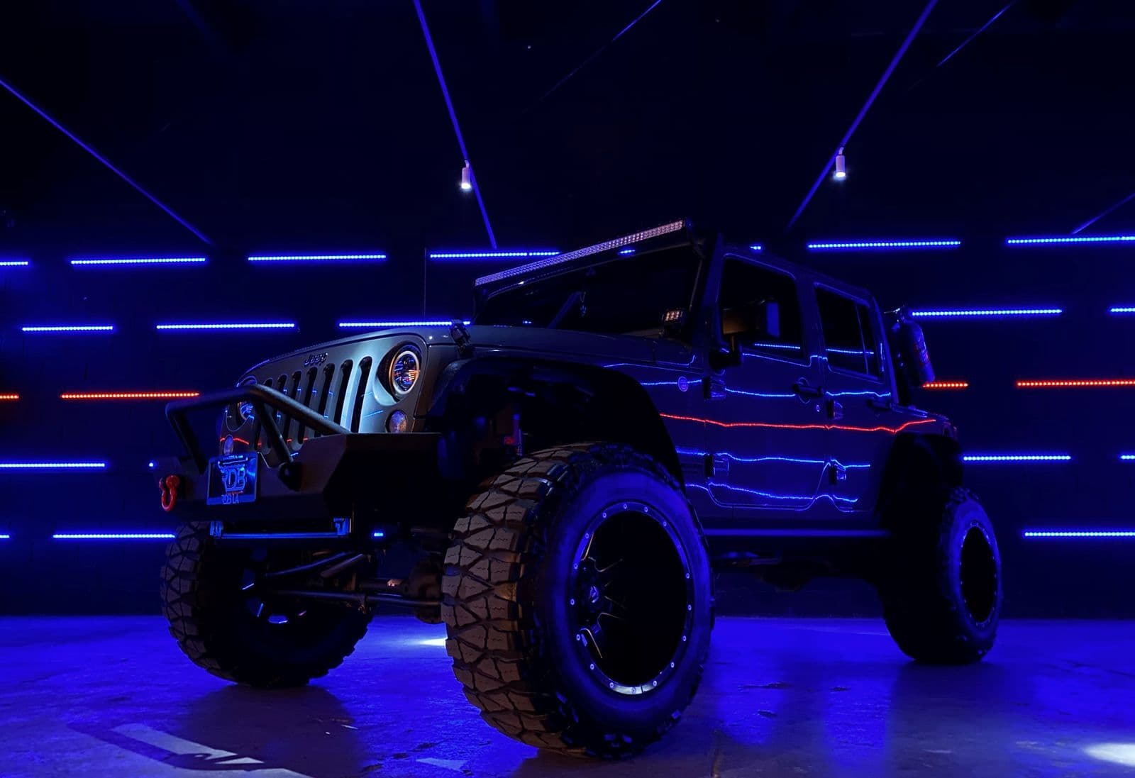 A lifted four-wheel drive on chunky mud-terrain tyres, lit by blue light strips in a dark garage.