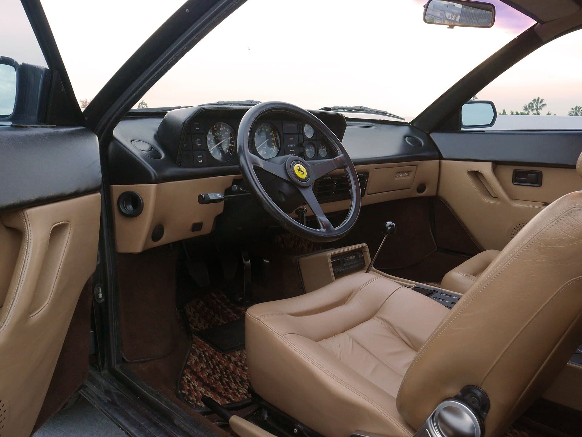 The interior of a 1988 Ferrari Mondial with the driver's door open, showing a metal gated gear shifter sitting in neutral.