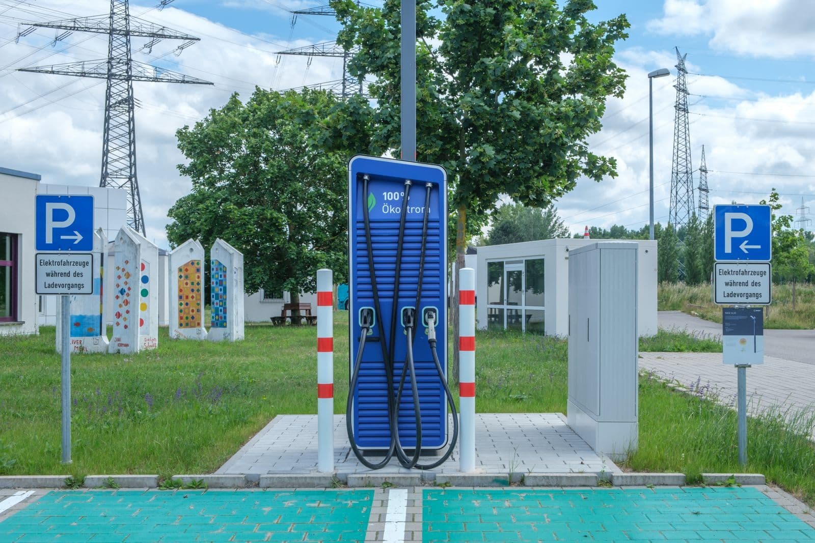 A blue DC rapid-charging pillar with three thick coiled cables, standing in an empty marked charging bay beside power pylons.